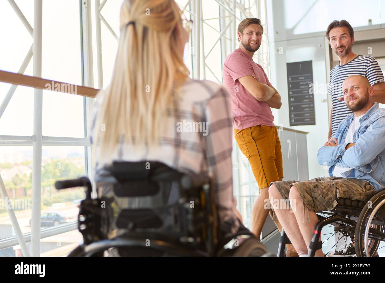 Eine vielfältige Gruppe von Freunden, die einen Rollstuhl benutzen, führt aktiv einen freundlichen Dialog in einer hellen Umgebung. Stockfoto