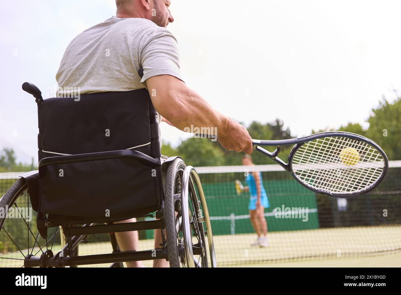 Eine aktive Person, die einen Rollstuhl benutzt, um im Freien ein Tennisspiel zu spielen, was Inklusion und Entschlossenheit veranschaulicht. Stockfoto