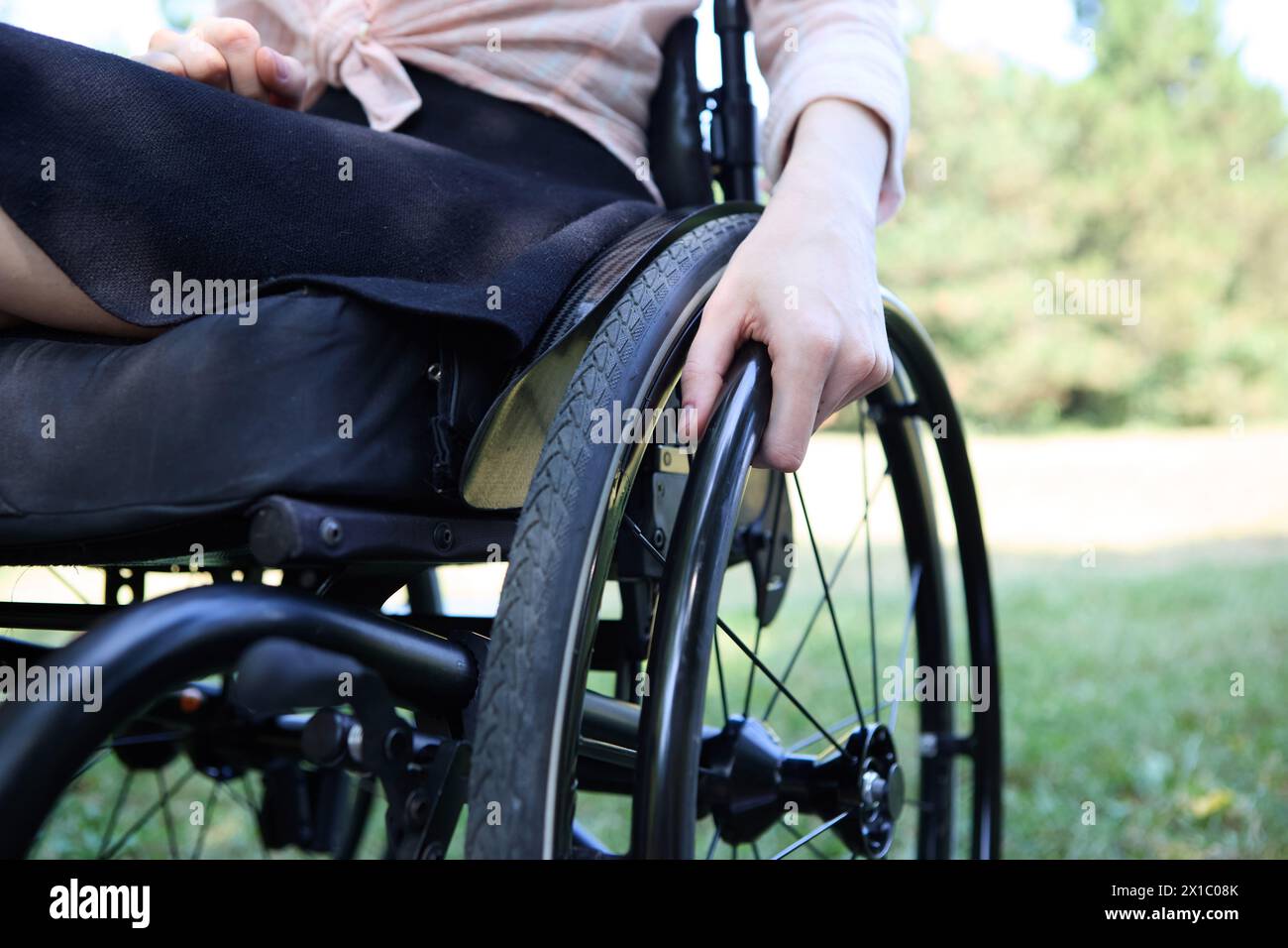 Nahaufnahme einer Person, die einen Rollstuhl in einem malerischen Park manövriert. Dieses Foto zeigt die Essenz von Barrierefreiheit und aktivem Lebensstil Stockfoto