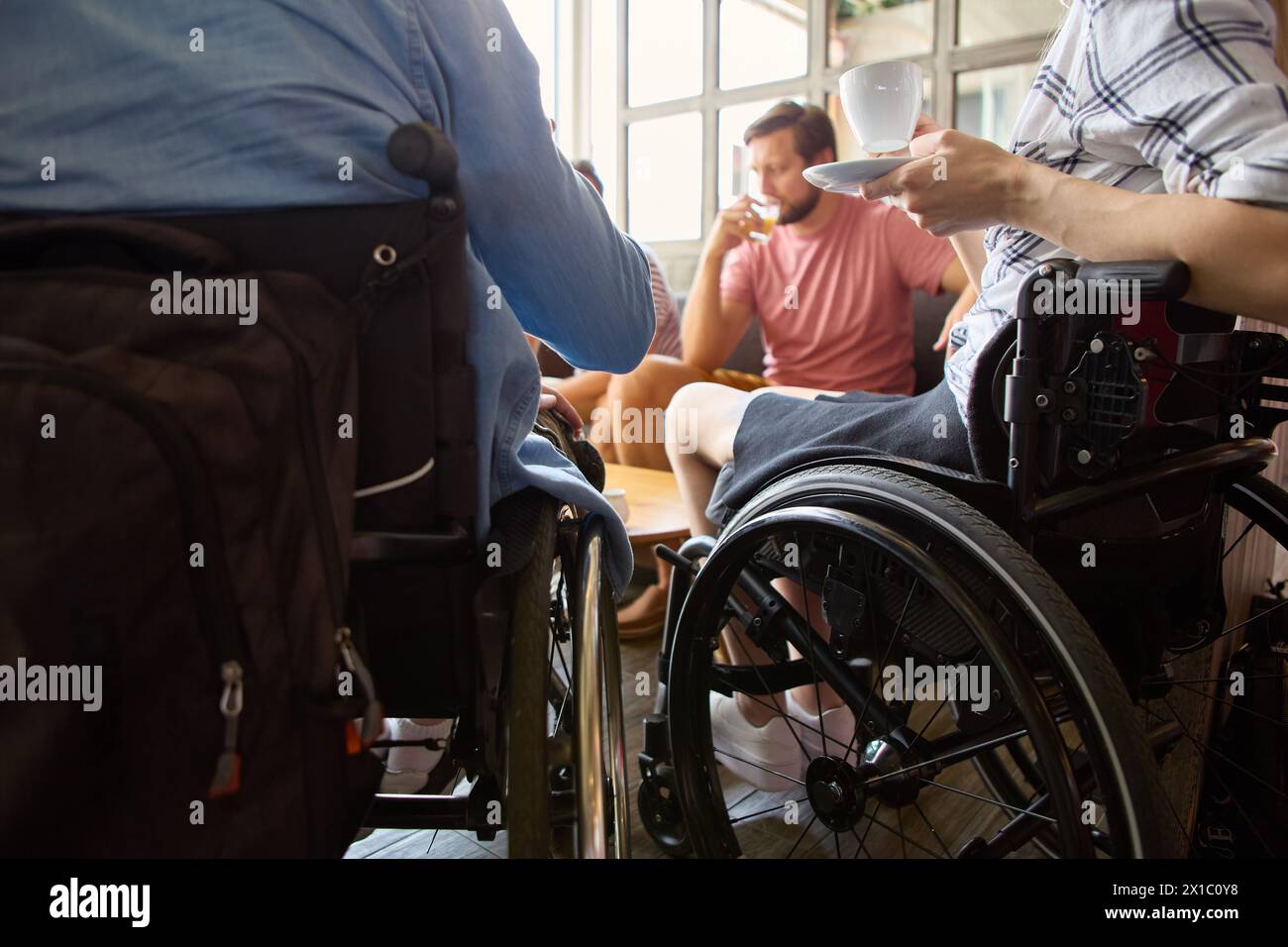 Ein zwangloses Meeting in einem cafÃ, bei dem eine Person mit Rollstuhl einen lebhaften Chat und Kaffee mit Freunden genießt. Stockfoto