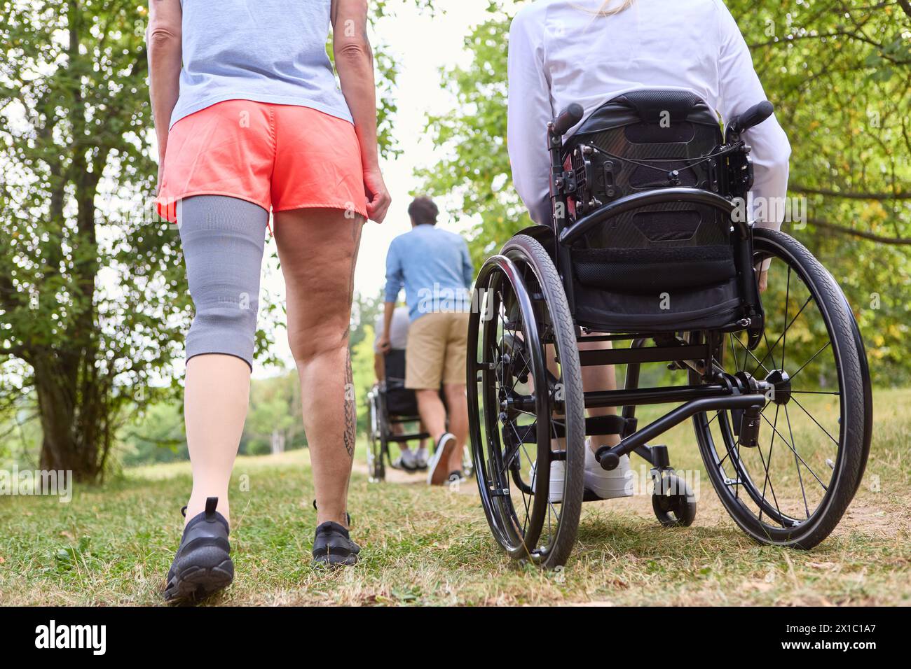 Eine inklusive Szene in einem Park mit zwei Freunden, einer mit Rollstuhl und einer mit einer Beinprothese, bei einem Spaziergang an einem sonnigen Tag. Stockfoto