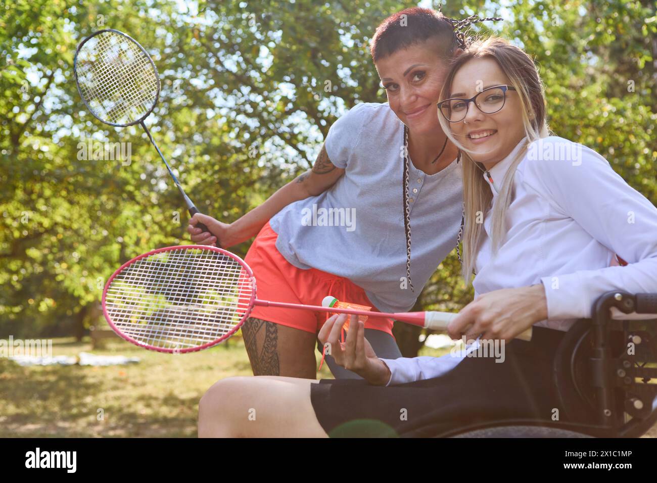 Eine Person im Rollstuhl spielt gerne Badminton mit einem stehenden Freund im Freien, was Inklusion und Anpassungsfähigkeit veranschaulicht. Stockfoto