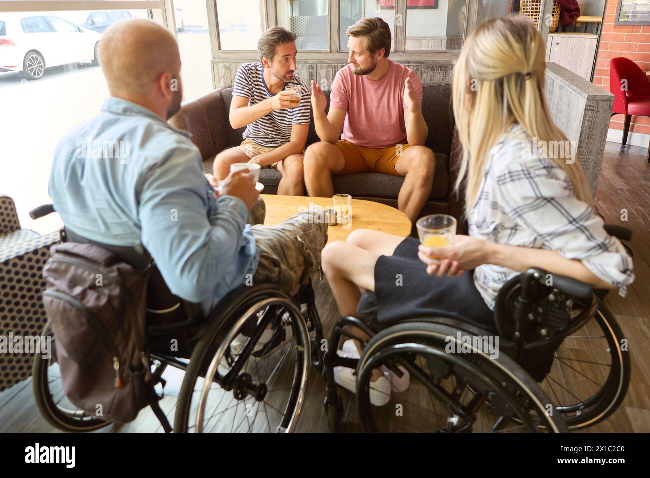 Eine vielfältige Gruppe von Freunden, darunter Einzelpersonen, die Rollstühle benutzen, unterhalten sich bei einem Drink in einem gemütlichen Café. Stockfoto