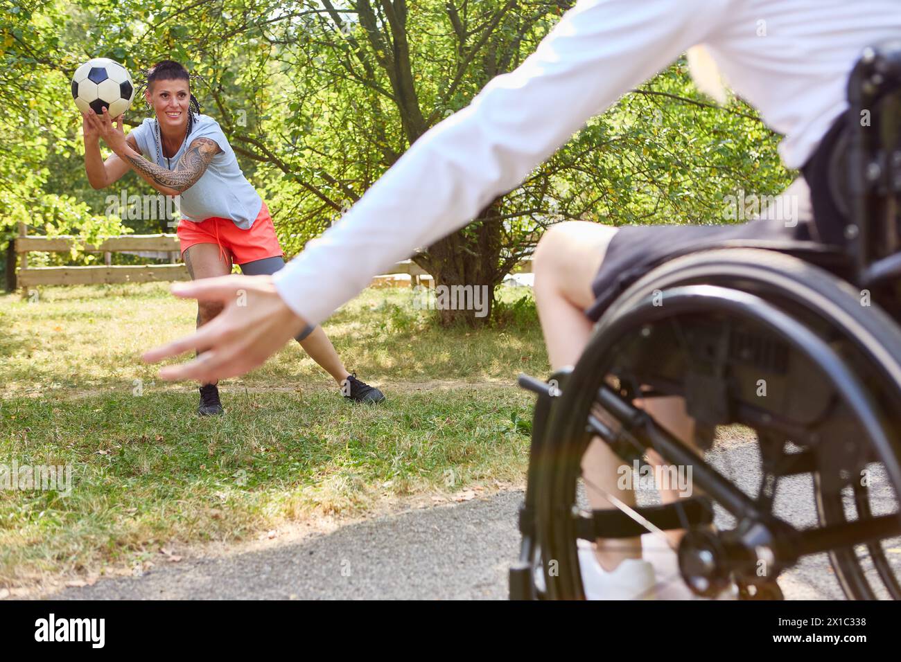 Eine inklusive Outdoor-Szene, in der eine Person mit Rollstuhl mit einer stehenden Person an einem Fußballspiel teilnimmt. Stockfoto