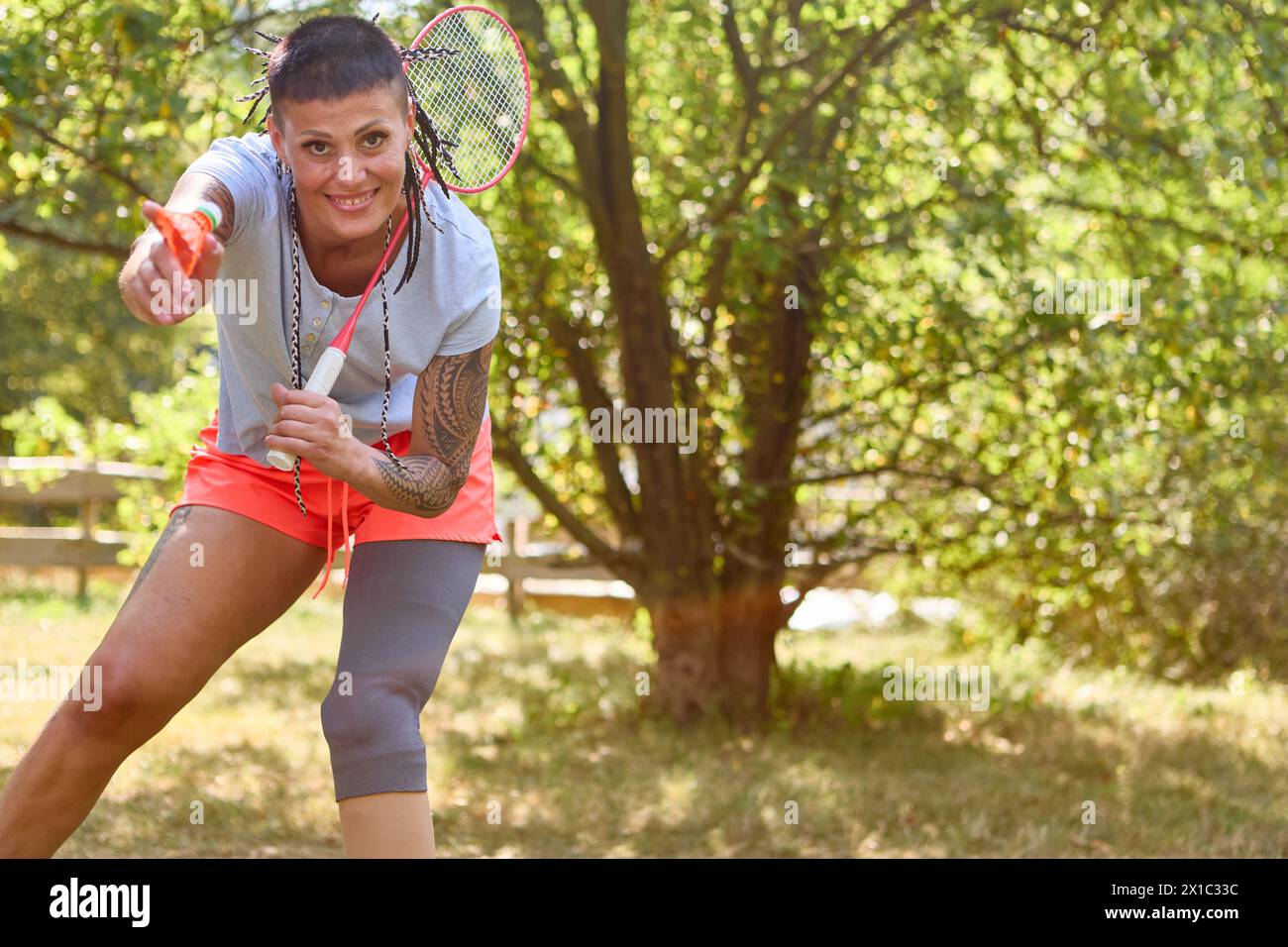 Eine befähigte Frau mit einer Beinprothese genießt eine Runde Badminton in einem üppigen Park. Sie zeigt Vitalität und Freude und steht für inklusiven Sport. Stockfoto