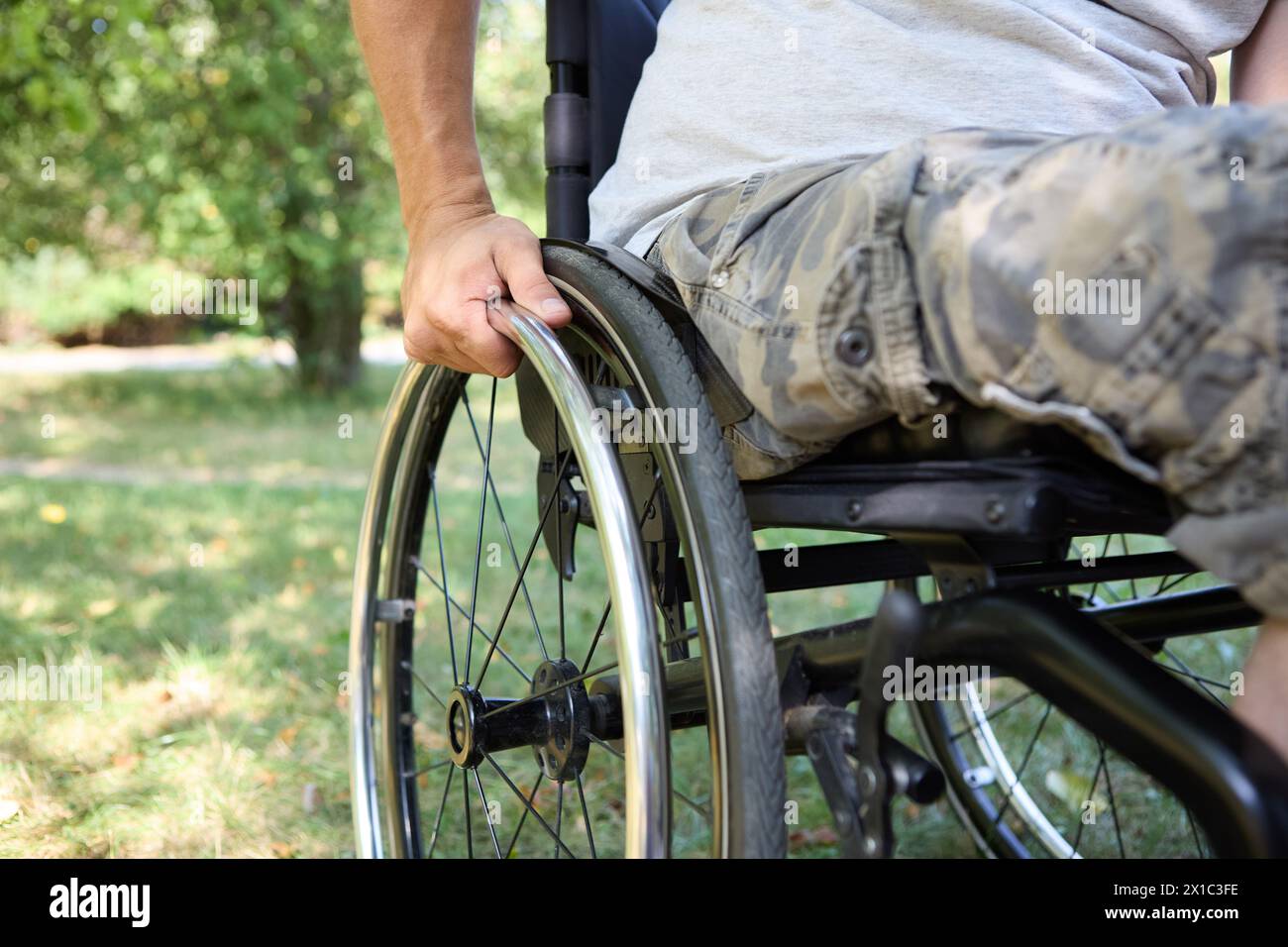 Eine Person, die einen Rollstuhl benutzt, wird im Freien festgehalten und konzentriert sich dabei auf unabhängige Mobilität und die Natur in einer ruhigen Parklandschaft. Stockfoto