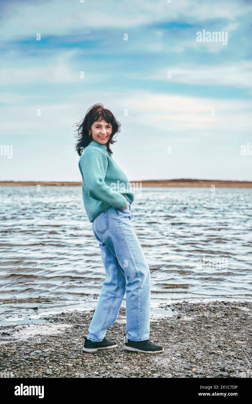49-jährige Russin im Pullover lachend, blickt an einem frühen Frühlingstag gegen das japanische Meer in die Kamera Stockfoto
