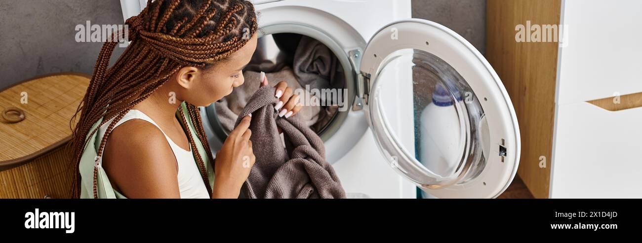 Eine afroamerikanische Frau mit Afro-Zöpfen sieht ihr Spiegelbild im Spiegel an, während sie im Badezimmer wäscht. Stockfoto