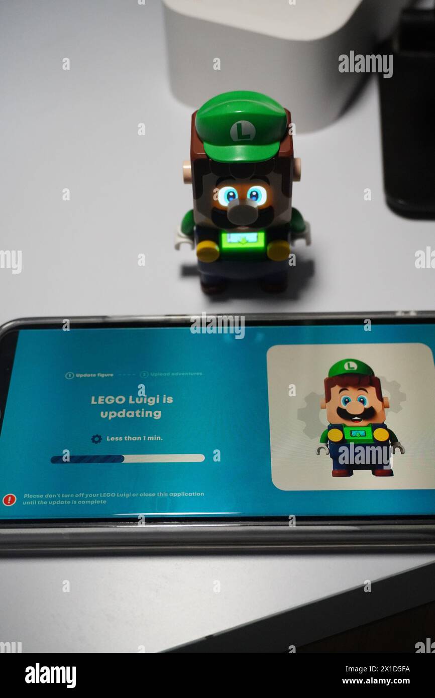 Eine Figur von Luigi aus dem Super Mario Bros-Zeichentrickfilm, die leuchtet und in der Nähe eines beleuchteten Mobiltelefons platziert wird Stockfoto
