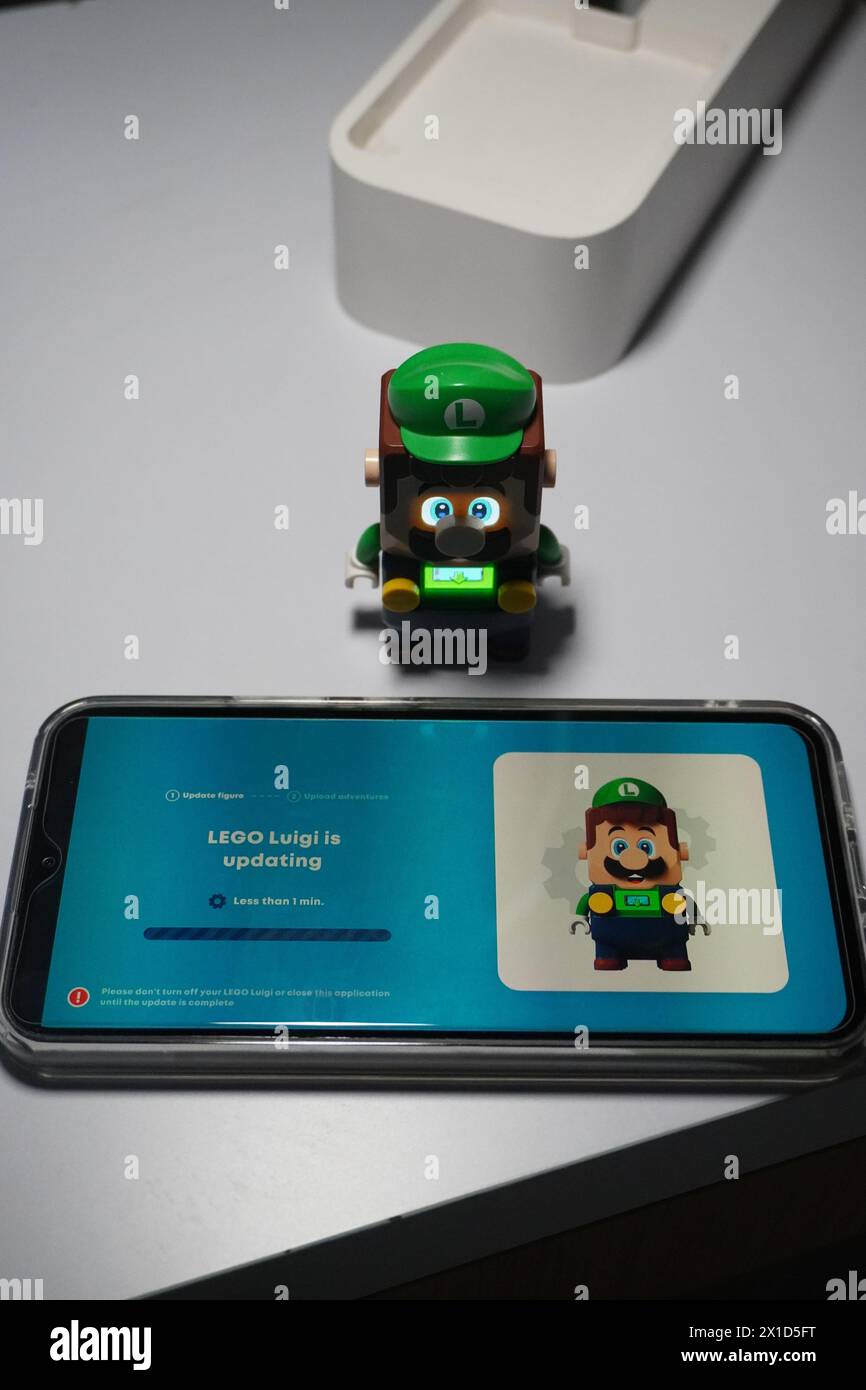 Eine Figur von Luigi aus dem Super Mario Bros-Zeichentrickfilm, die leuchtet und in der Nähe eines beleuchteten Mobiltelefons platziert wird Stockfoto
