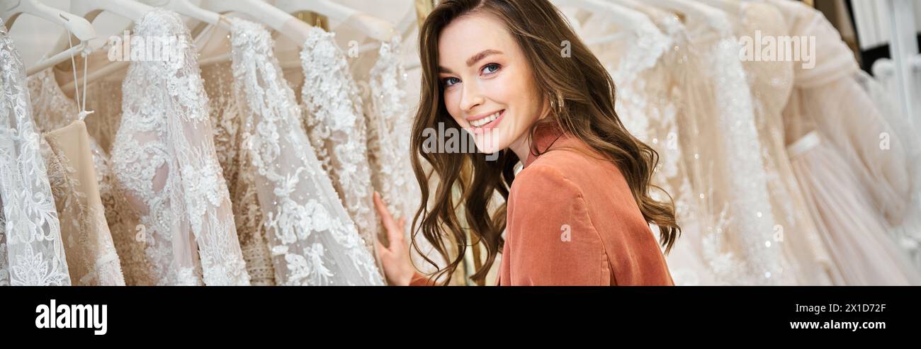 Eine junge Braut steht vor einer Auswahl von Brautkleidern und versucht, das perfekte Kleid für ihren besonderen Tag zu finden. Stockfoto