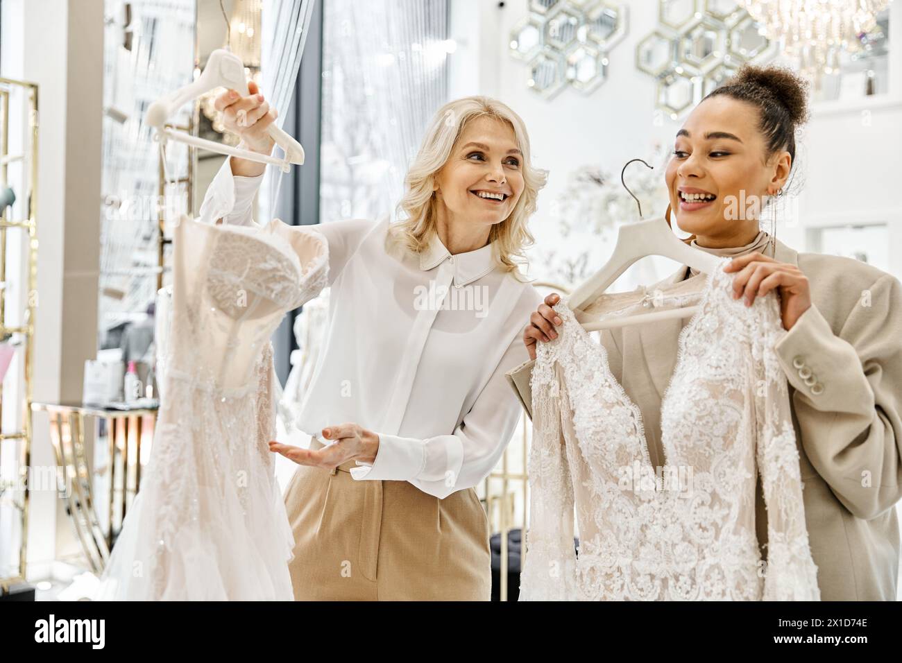 Junge Frauen, eine schöne Braut, die Kleider in einem Laden hochhält, unterstützt von einem Ladenleiter. Stockfoto