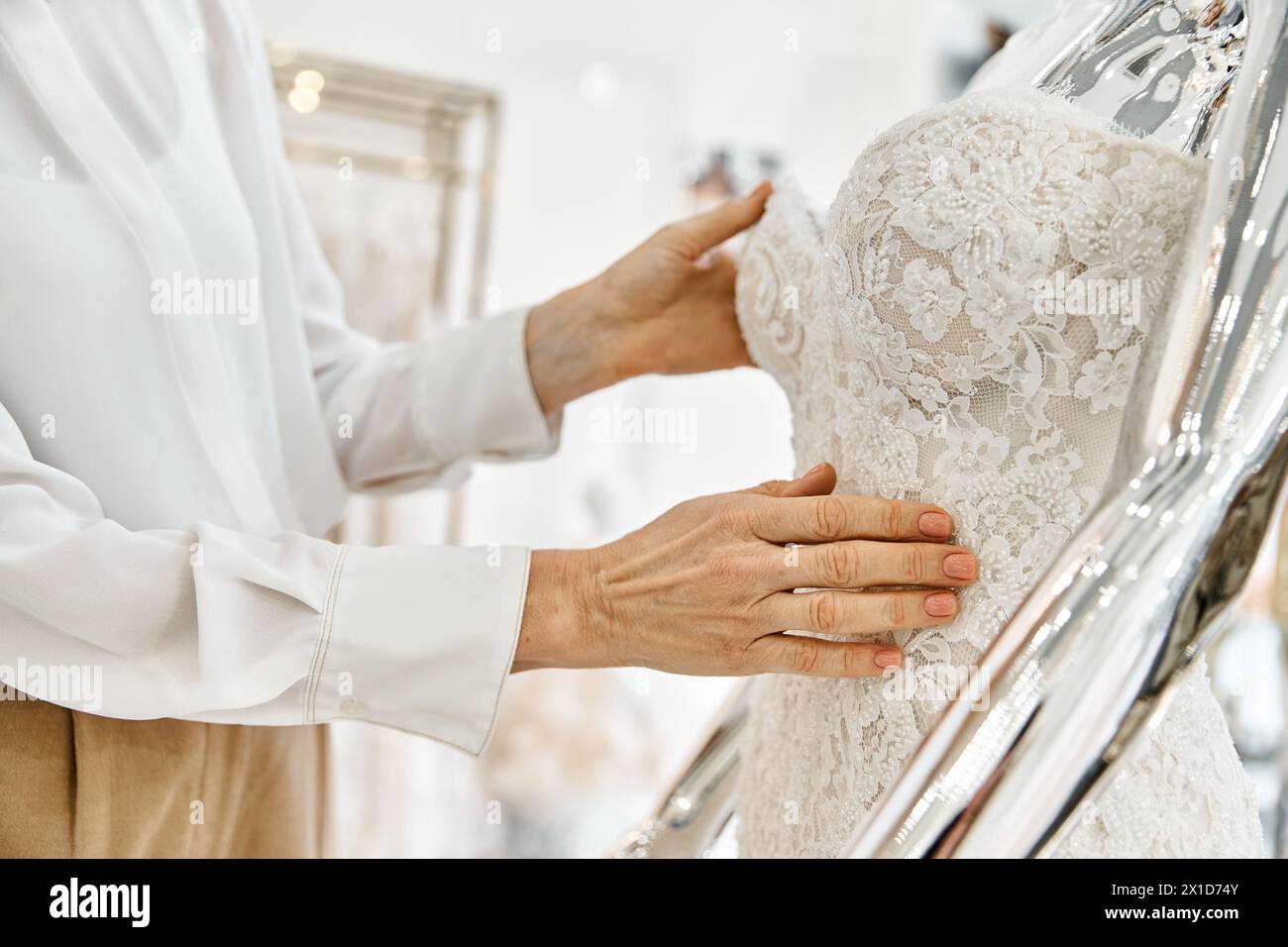 Ein Einkaufsassistent mittleren Alters steht selbstbewusst vor einem Regal mit eleganten Kleidern in einem Hochzeitssalon. Stockfoto