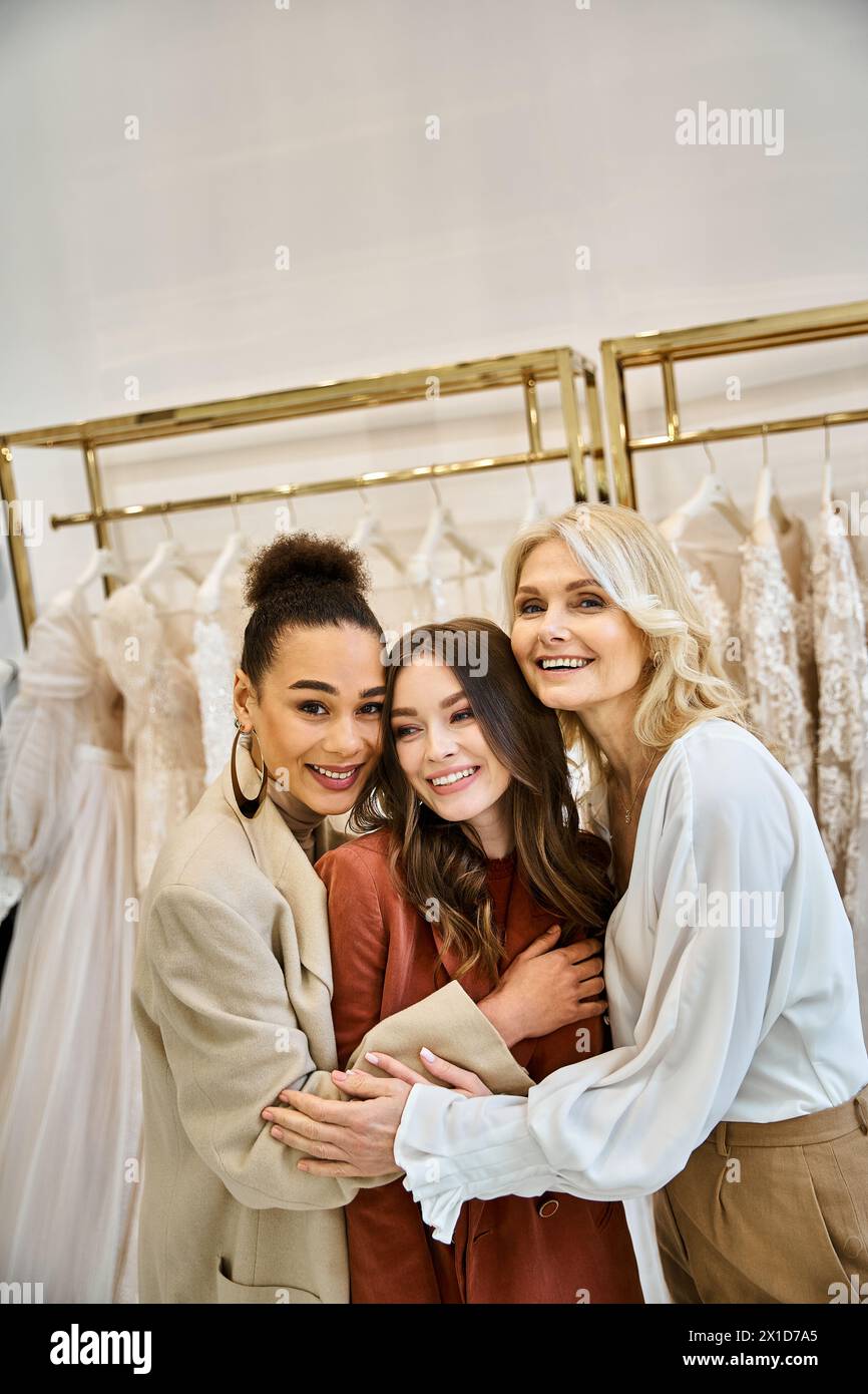 Drei Frauen, darunter eine junge Braut, ihre Mutter und beste Freundin, stehen vor einem Regal mit atemberaubenden Brautkleidern. Stockfoto