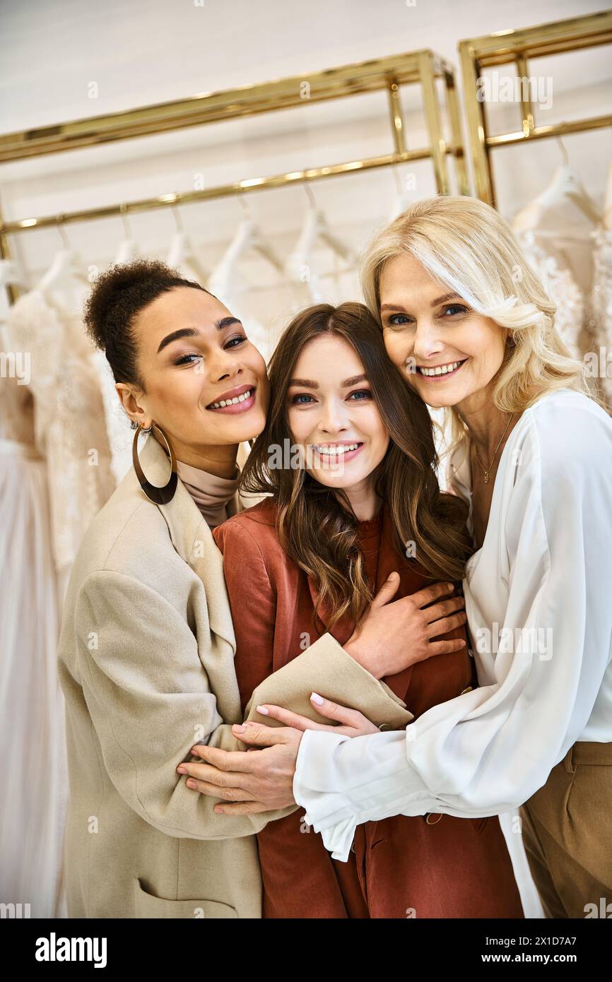 Drei Frauen – eine Braut, ihre Mutter und beste Freundin – stehen zusammen und wählen Kleider aus einem Regal aus. Stockfoto
