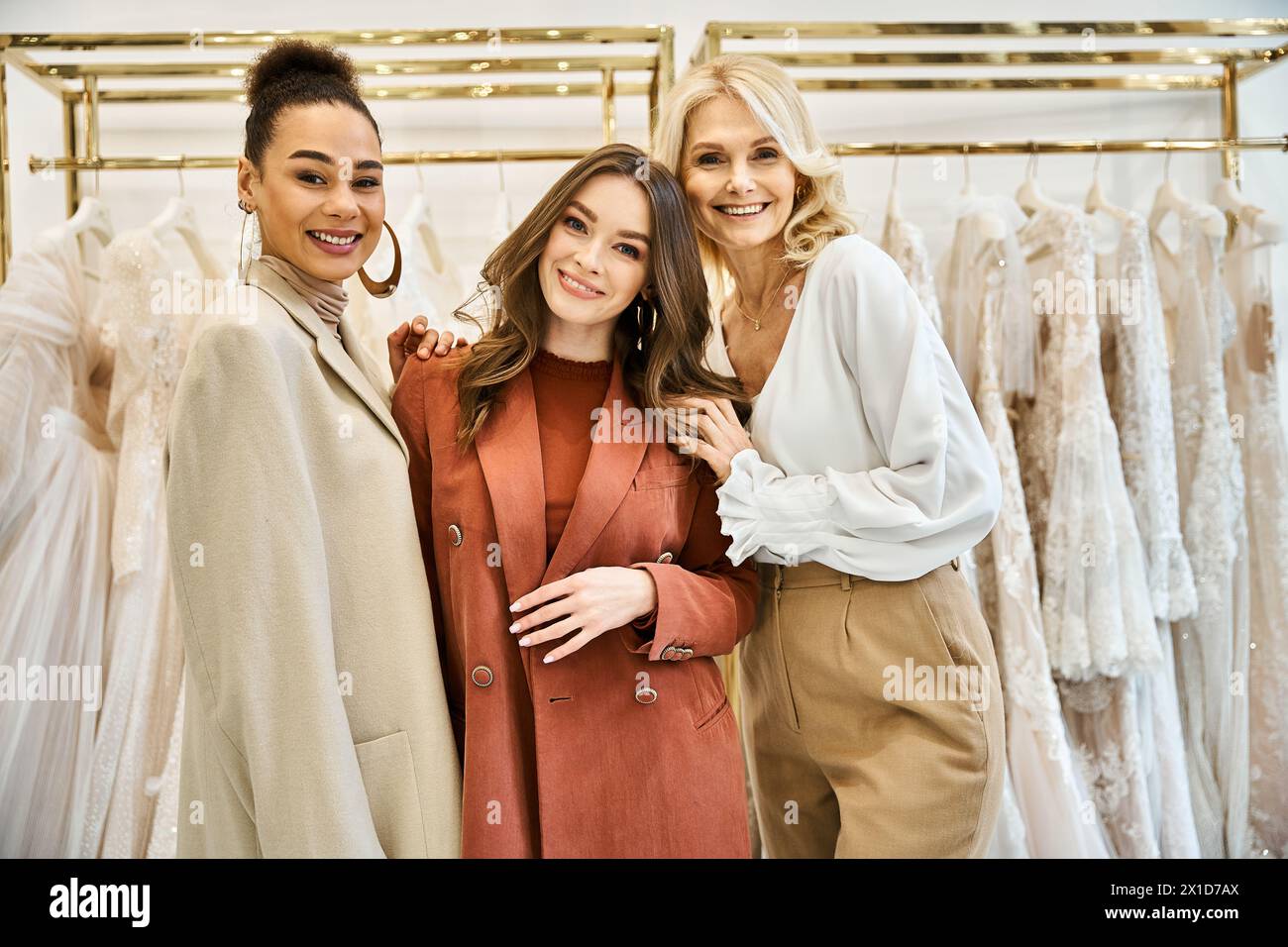 Eine junge Braut, ihre Mutter und ihre beste Freundin stehen neben einem Kleiderständer und kaufen das perfekte Hochzeitskleid. Stockfoto