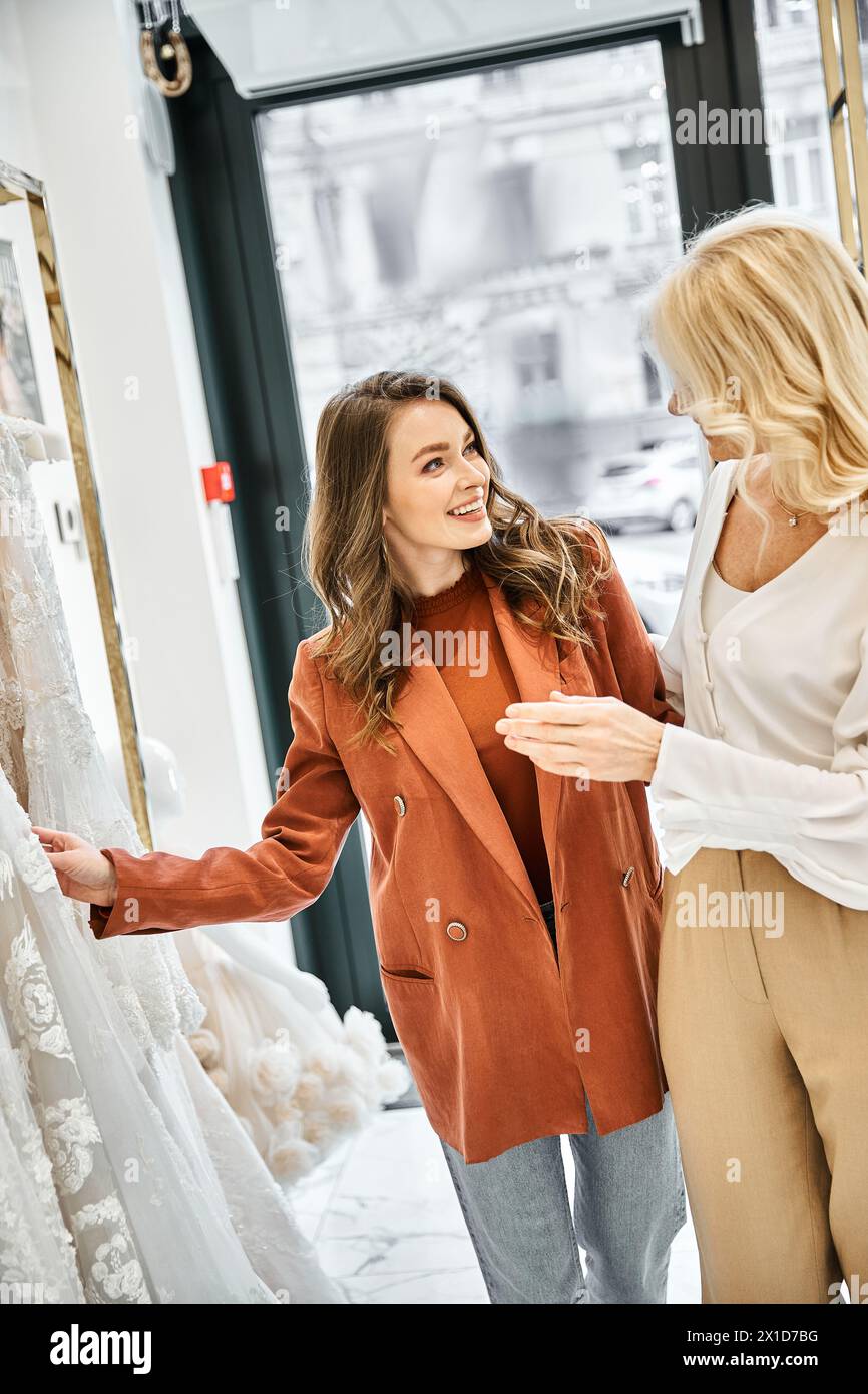 Zwei Frauen, eine junge schöne Braut und ihre Mutter, stöbern und probieren Brautkleider in einem Laden voller Brautkleider aus. Stockfoto