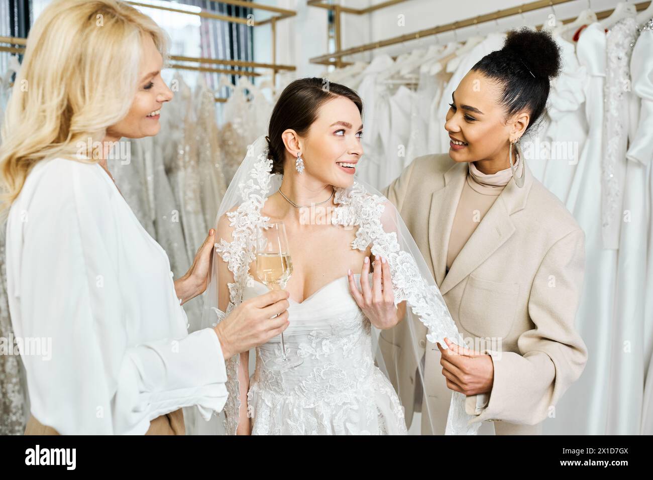 Eine junge Braut, ihre Mutter und die Brautjungfer stehen in einem Brautsalon neben einem Kleiderständer und prüfen ihre Optionen. Stockfoto