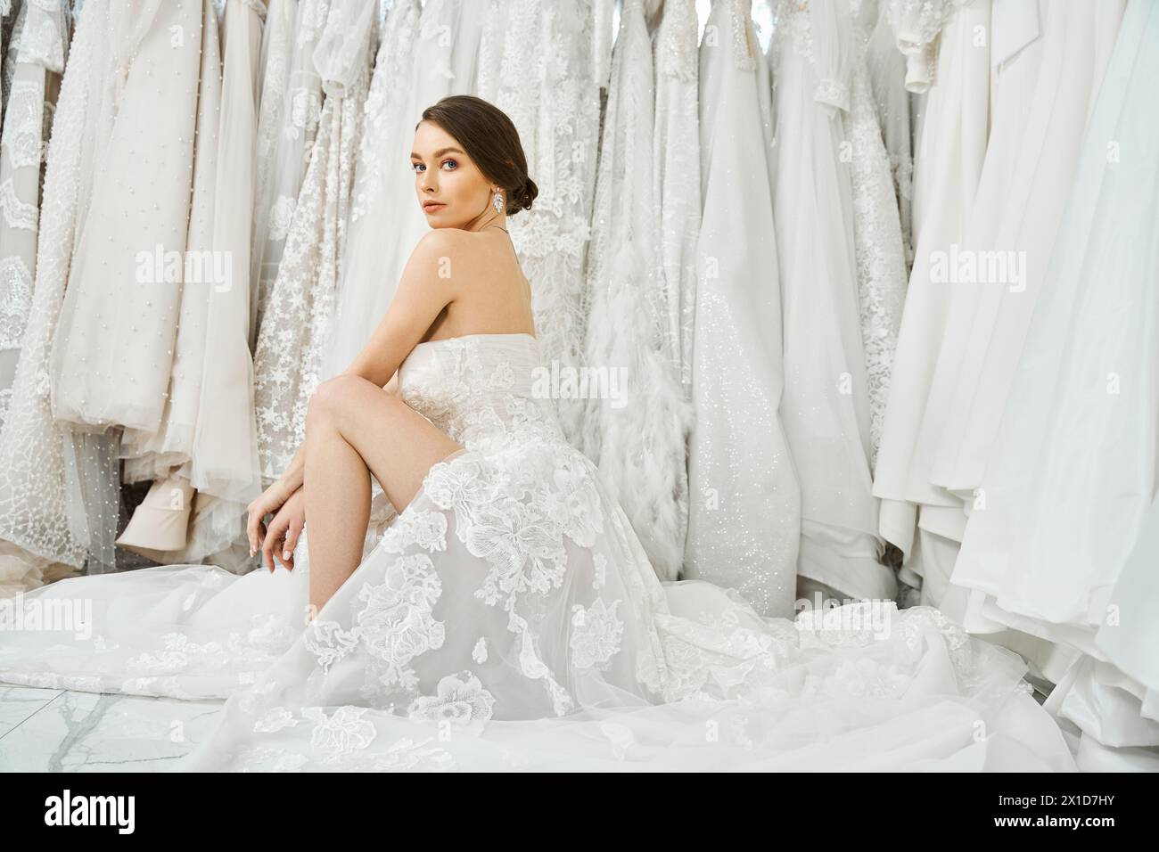 Eine junge brünette Braut sitzt vor einem Kleiderständer und wählt sorgfältig das perfekte Kleid für ihren Hochzeitstag aus. Stockfoto