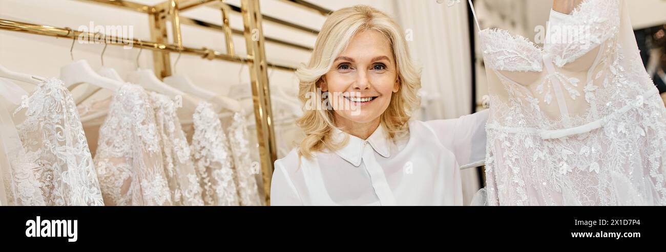 Ein wunderschöner Einkaufsassistent mittleren Alters stöbert in einem Salon in verschiedenen Brautkleidern. Stockfoto