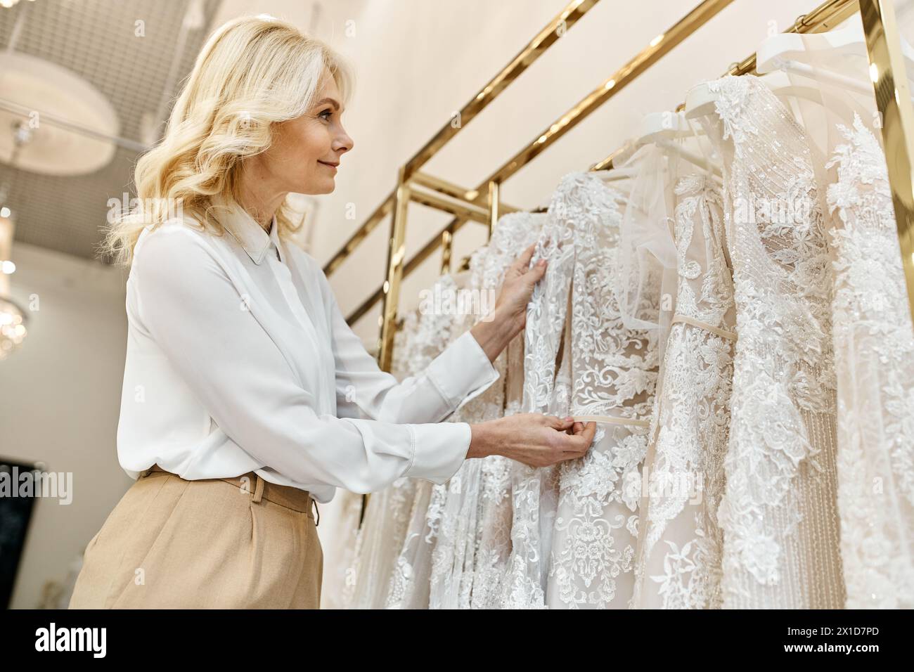 Ein hübscher Einkaufsassistent mittleren Alters hilft einer Frau, die Brautkleider auf einem Regal in einem Brautsalon durchzustöbern. Stockfoto