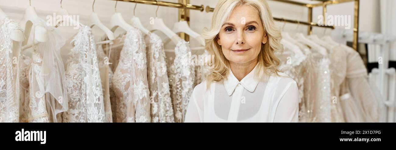 Wunderschöner Einkaufsassistent mittleren Alters, der vor einem Kleiderständer in einem Hochzeitssalon steht. Stockfoto