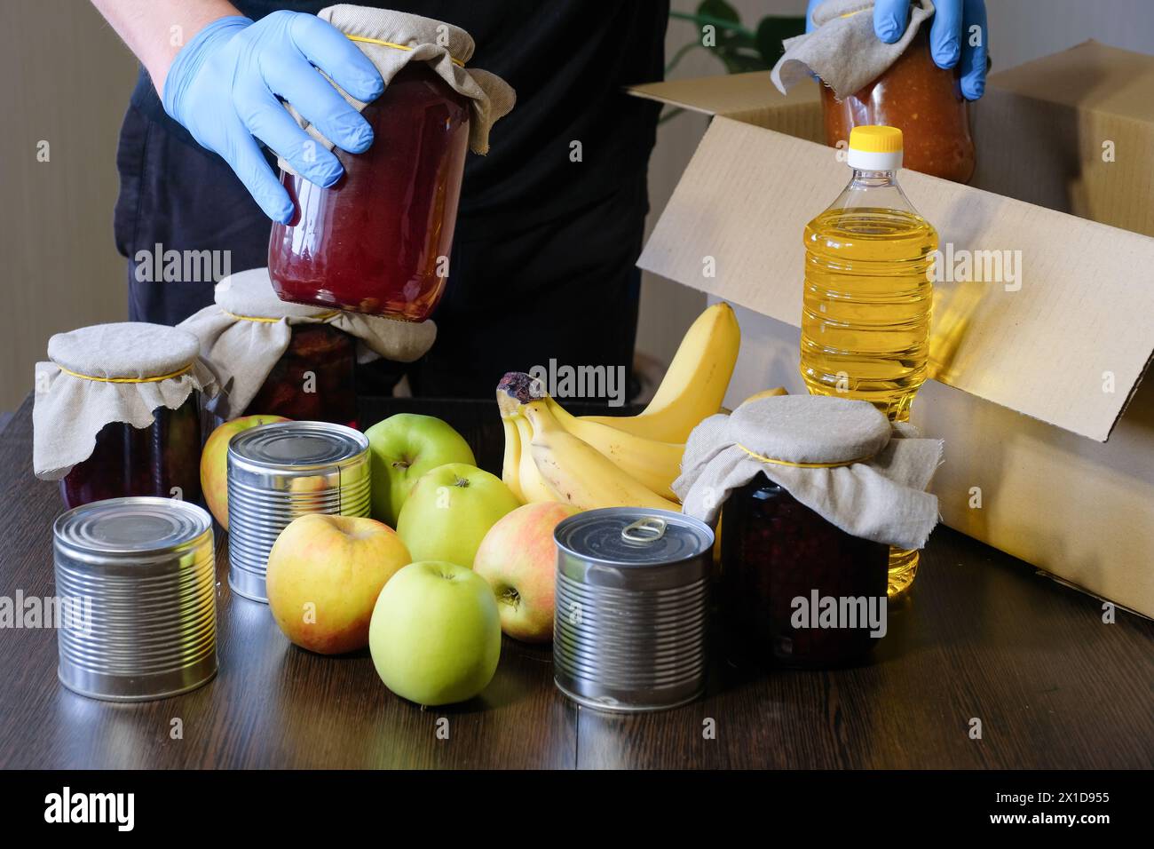 Ein Freiwilliger mit Schutzhandschuhen verpackt Lebensmittel in eine Kiste. Nahrungsmittellieferdienste während der Coronavirus-Pandemie Stockfoto
