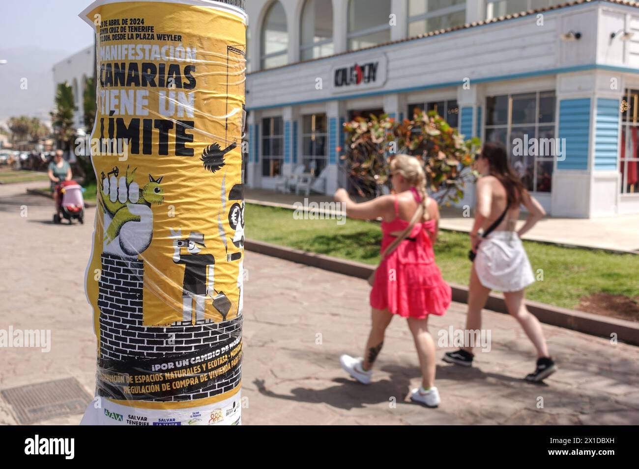 Los Cristianos, Teneriffa, 16. April 2024 - Touristen laufen an Anti-Touristen-Plakaten entlang der Strandfront in Los Cristianos vorbei. Auf dem Poster steht, dass die Kanarischen Inseln eine Grenze haben. Die gelben Schilder werben für den anti-touristischen Protest am Samstag, den 20. April. In Santa Cruz de Teneriffa. Parken ist auch ein großes Problem in der Gegend, da unzählige Besucher Tausende von Plätzen füllen, was für die Bewohner und Besucher gleichermaßen Kopfschmerzen bereitet. Quelle: Stop Press Media/Alamy Live News Stockfoto