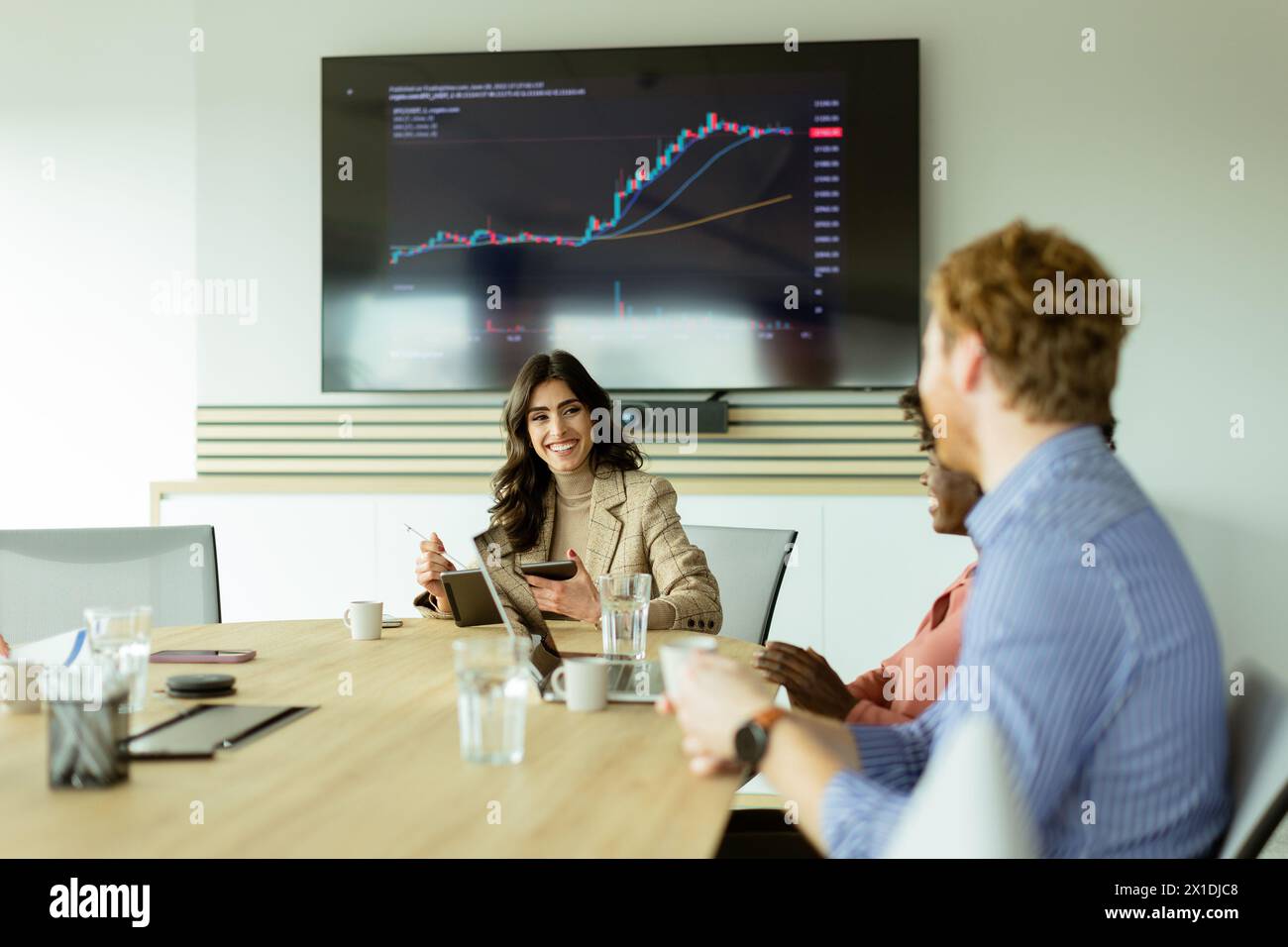 Das Team nimmt aktiv an einem Geschäftstreffen Teil, wobei ein Börsendiagramm auf einem Monitor angezeigt wird. Stockfoto