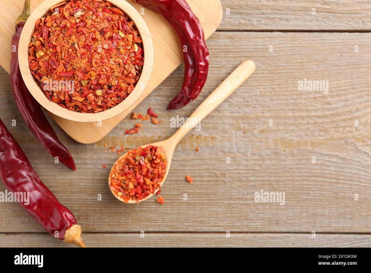 Aromatisches Gewürz. Rote Chilischoten in Schüssel, Löffel und Schoten auf Holztisch, flach gelegt. Leerzeichen für Text Stockfoto