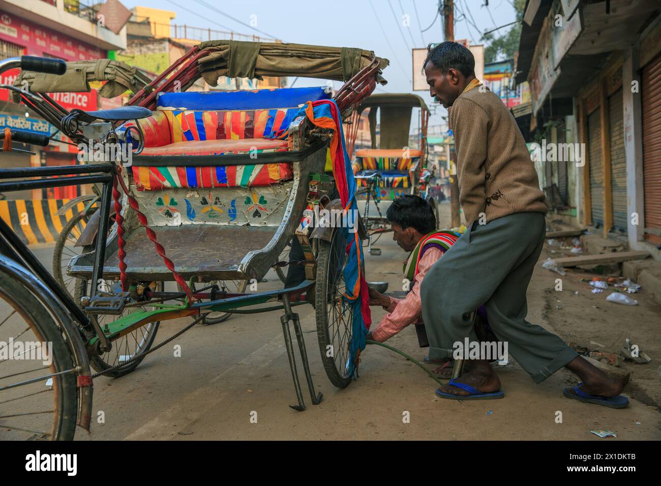 Zwei Rad-Rikscha-Fahrer, die einen Platten Reifen auf einer Fahrrad-Rikscha in Varanasi, Indien, aufpumpen Stockfoto
