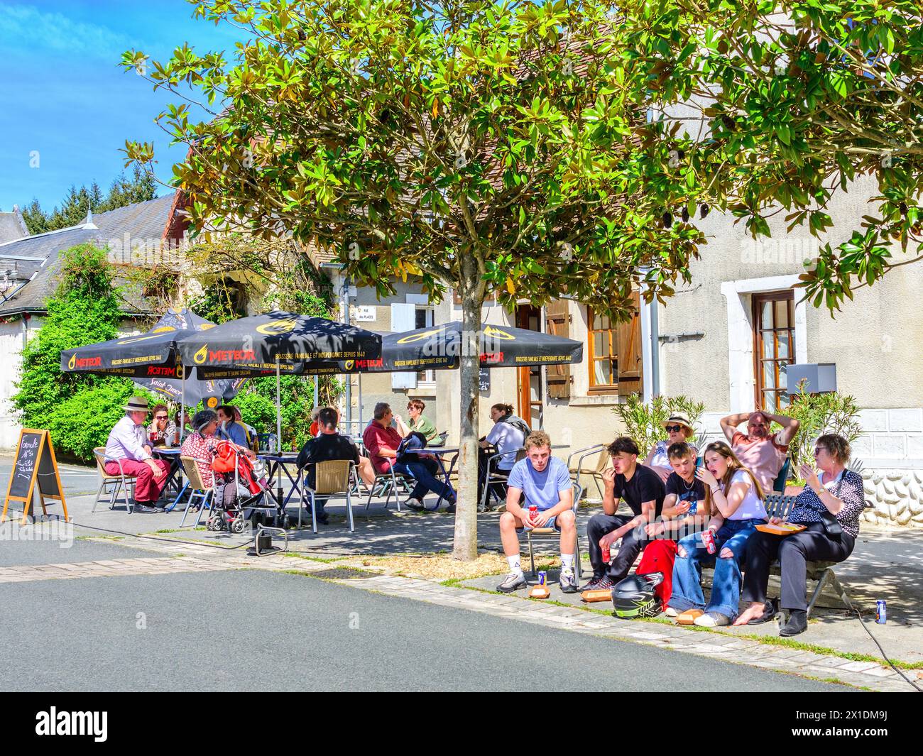 Sonntagsmittagsgruppen essen und trinken im Schatten von Bäumen und Sonnenschirmen - Le Blanc, Indre (36), Frankreich. Stockfoto