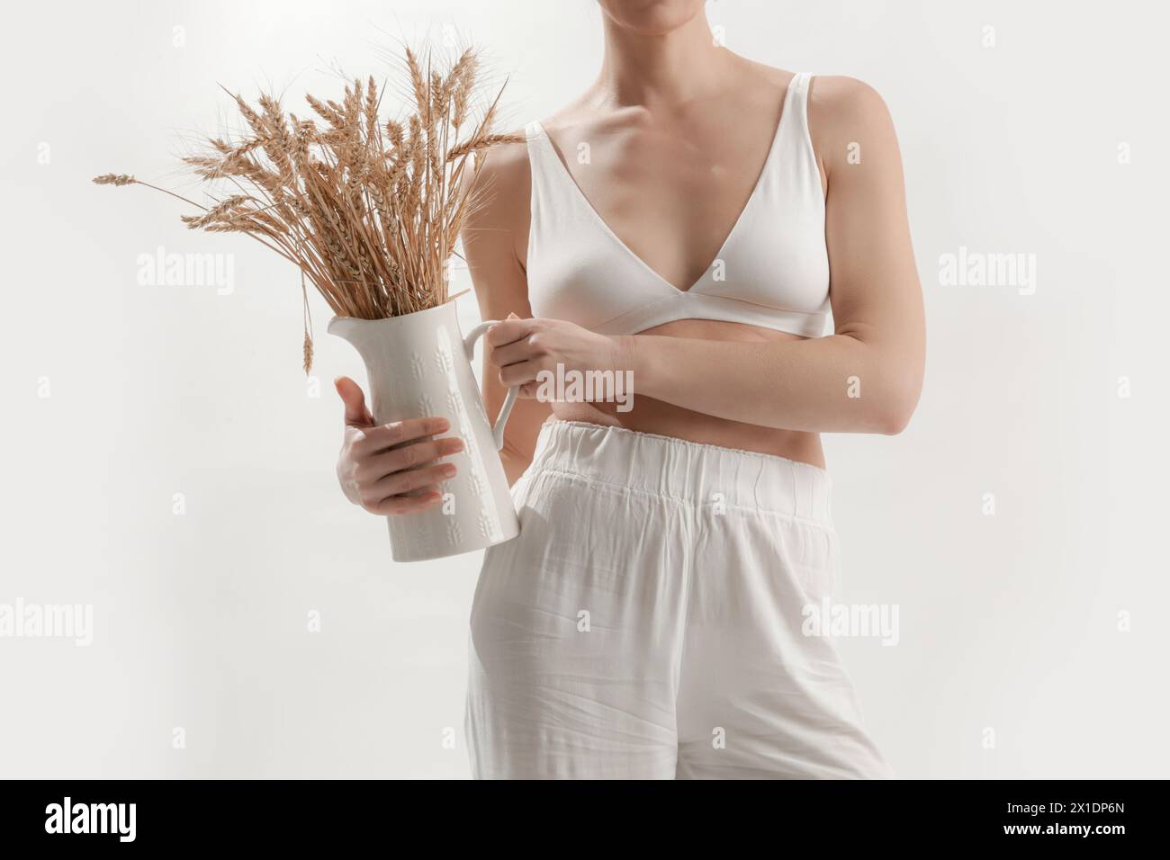 Junge Frau, die Keramikkrug mit Weizenstacheln hält, Zöliakie und Glutenunverträglichkeit Stockfoto