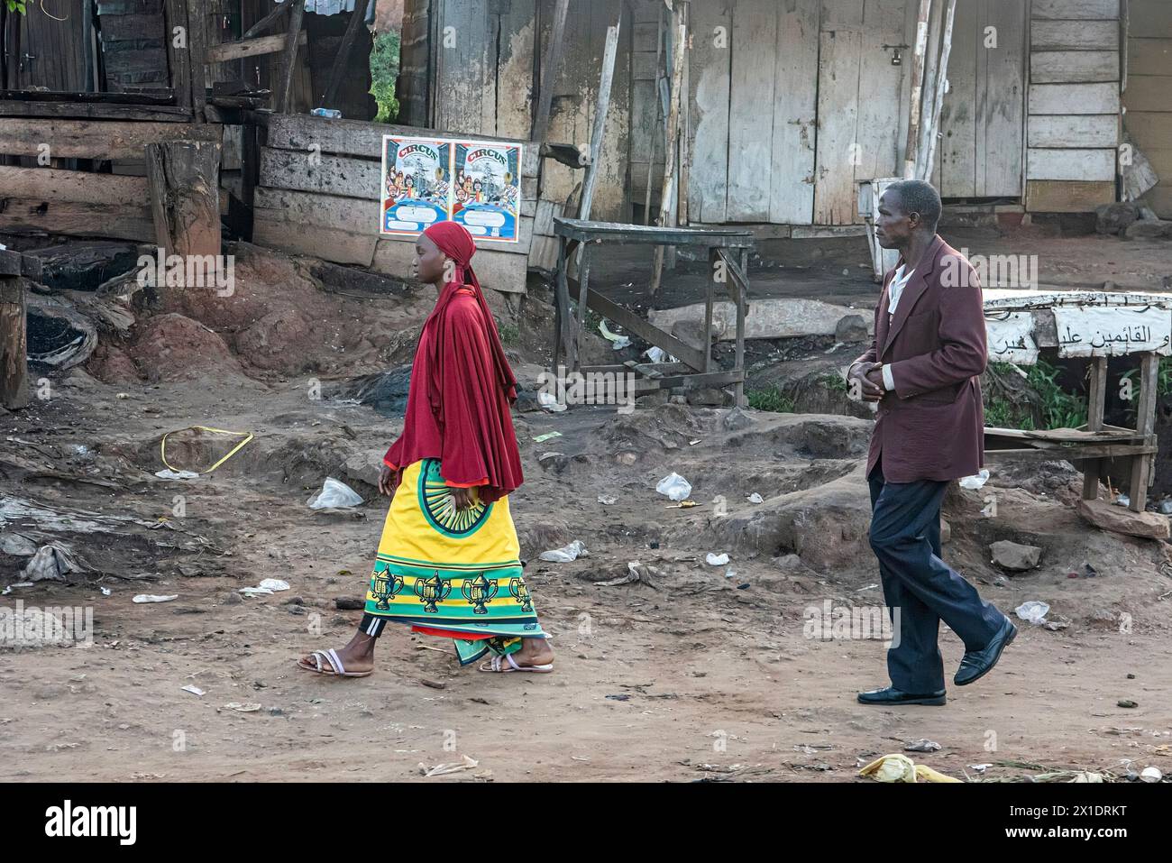 Ein ugandischer Vater und sein Sohn, beide in traditioneller Kleidung, schlendern durch die lebhaften Straßen von Kampala, der Sohn in einem bunten Gelb geschmückt Stockfoto