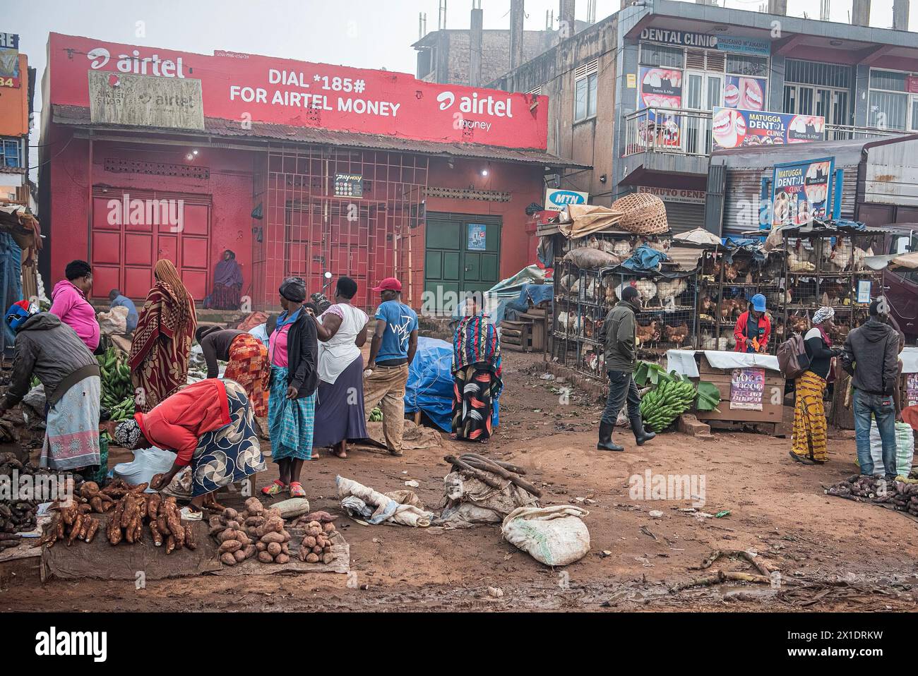 Ein lebhafter Straßenmarkt in Kampala, Uganda, mit bunt gekleideten Händlern, die Obst, Gemüse, Geflügel und mehr verkaufen. Eine Zahnklinik und ein Telefon Stockfoto
