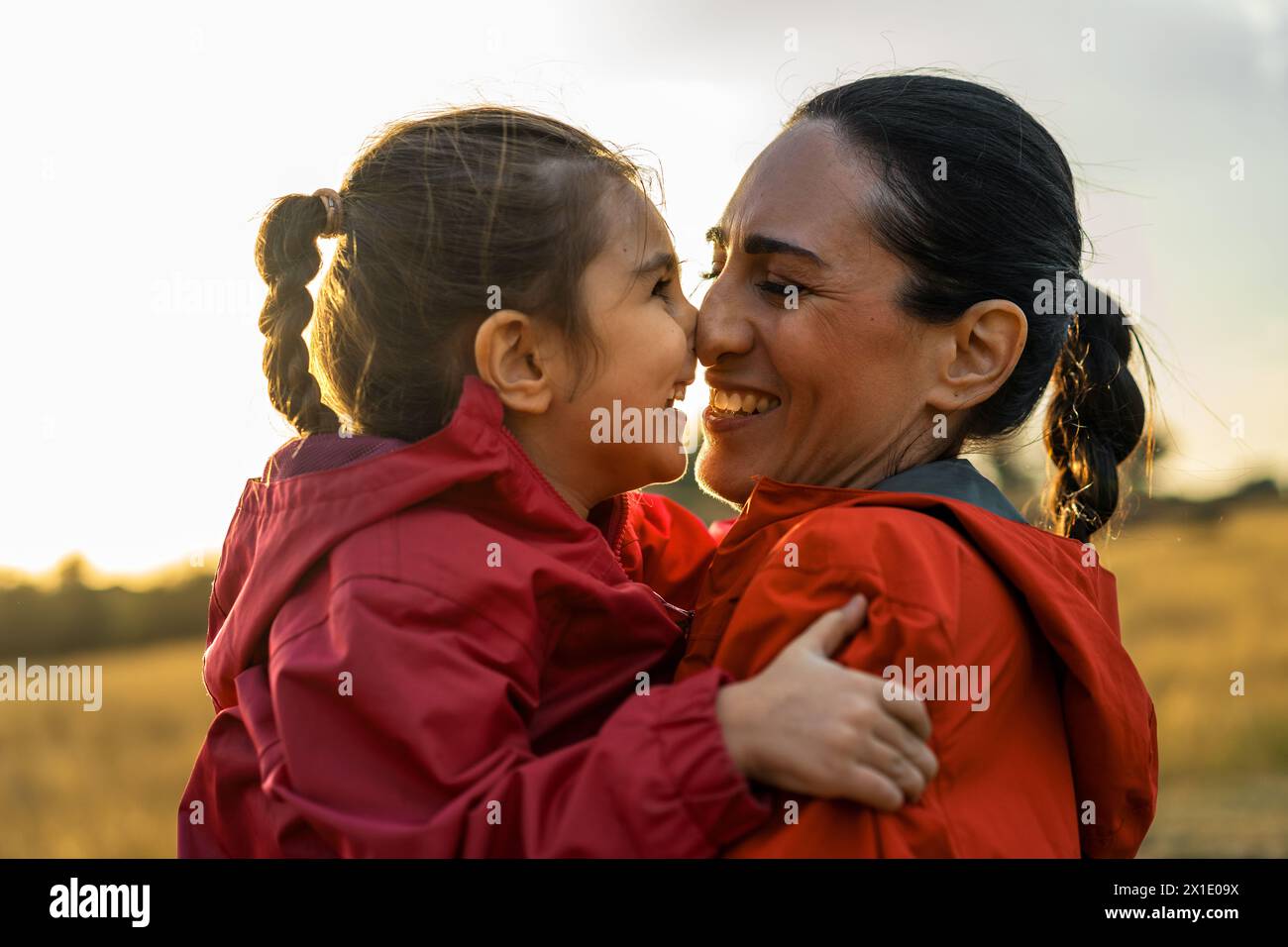 Eine Mutter und Tochter tauschen ein Lächeln voller Liebe aus, umhüllt in den goldenen Glanz des Sonnenuntergangs während eines gemeinsamen Moments auf dem Land. Stockfoto