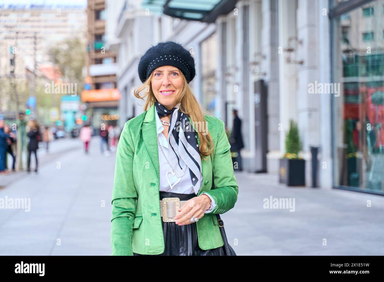 Eine Frau mittleren Alters trägt modische Kleidung und einen Hut, der die Straße hinunter läuft Stockfoto