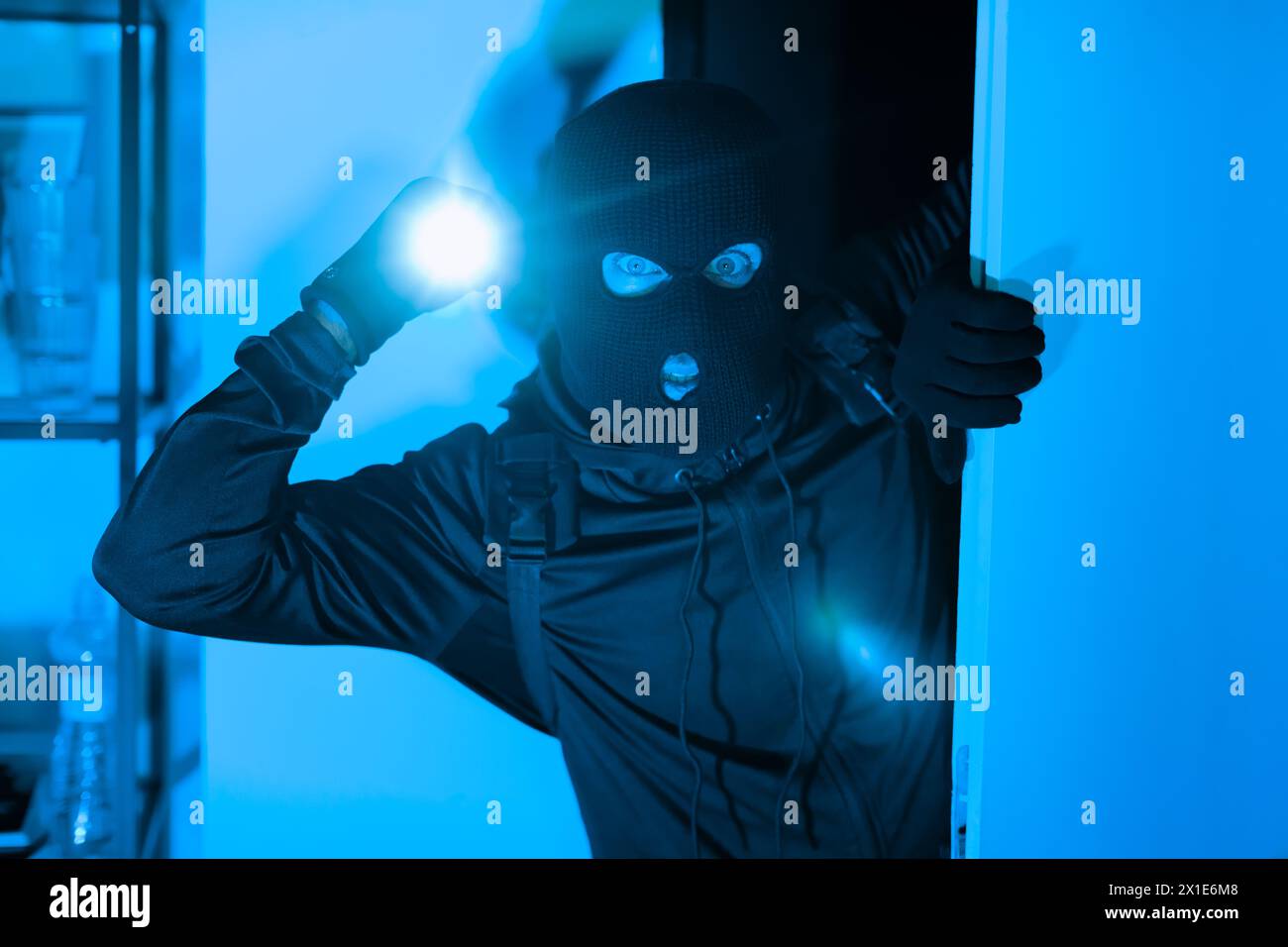 Einbrecher mit Taschenlampe, die sein Gesicht in einem dunklen Raum beleuchtet Stockfoto