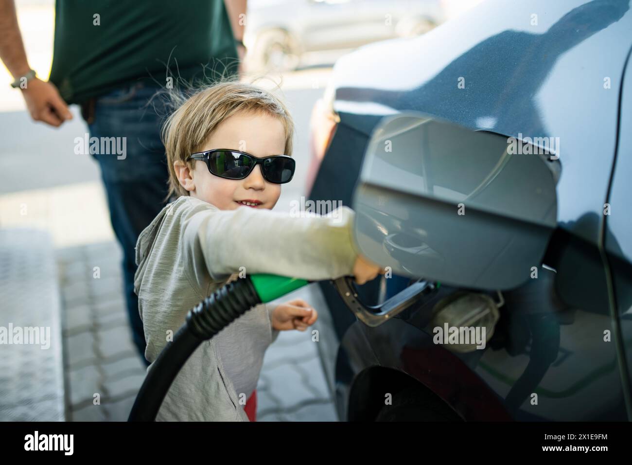 Süßer kleiner blonder Junge, der eine Pumpdüse hält. Kleiner, lustiger Junge, der Vater hilft, das Auto an einer Tankstelle zu tanken. Papas kleiner Helfer. Stockfoto