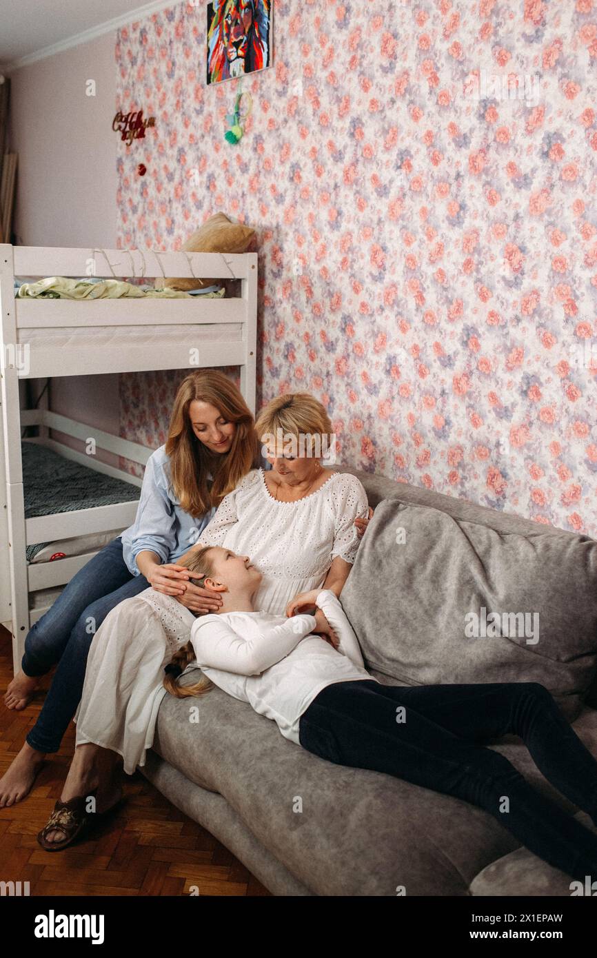 Zwei Frauen sitzen auf einer Couch, eine hält ein Baby. Die Frauen wirken entspannt, wenn sie mit dem Baby interagieren. Stockfoto