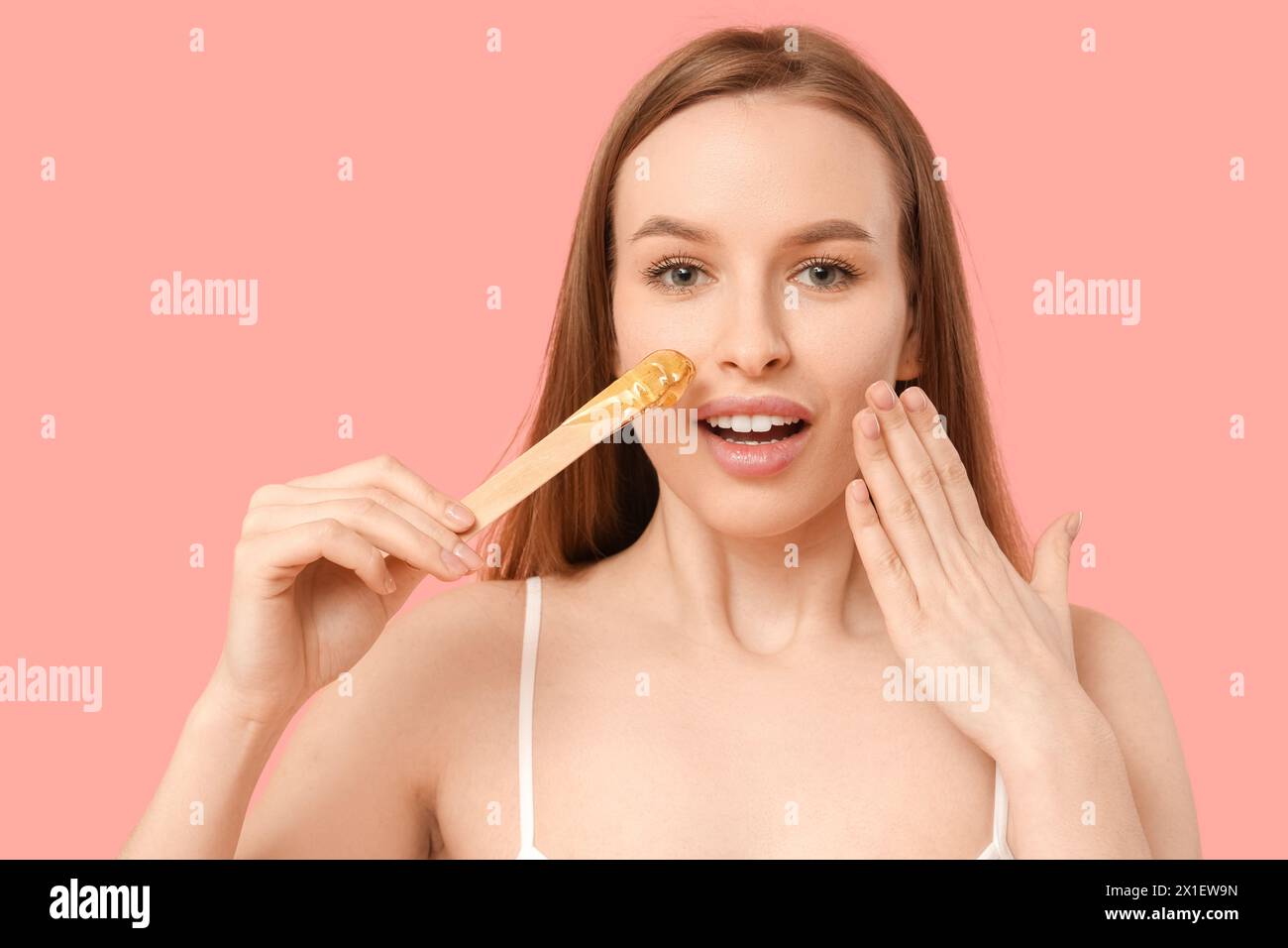 Schöne junge schockierte Frau, die Spachtel mit Zuckerpaste auf rosa Hintergrund hält Stockfoto