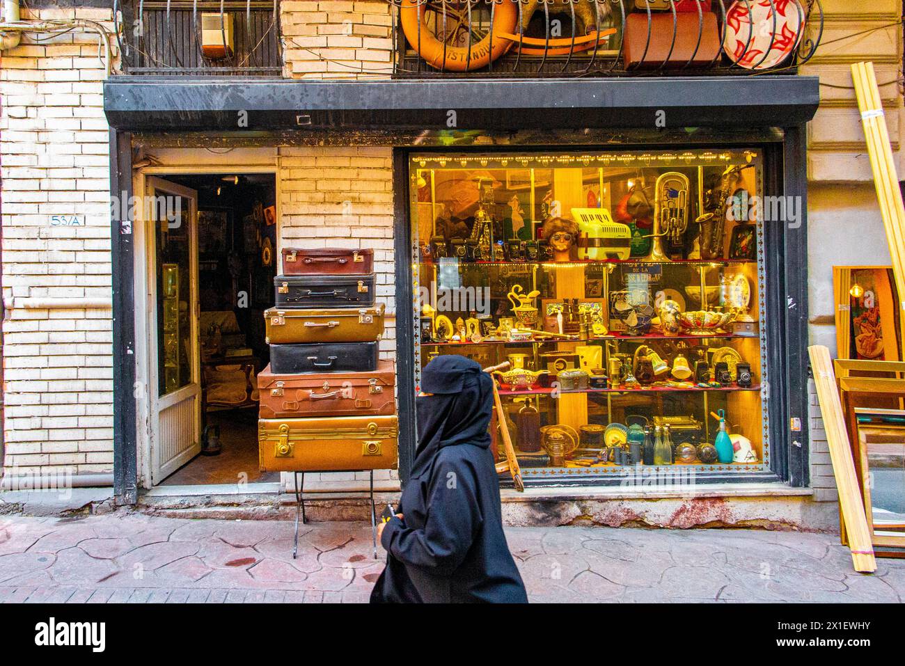 Eine Dame in einer Burka läuft an einem Antiquitätenladen in Istanbul vorbei, mit hoch gestapelten Vintage-Koffern und Kuriositäten im Schaufenster. Stockfoto