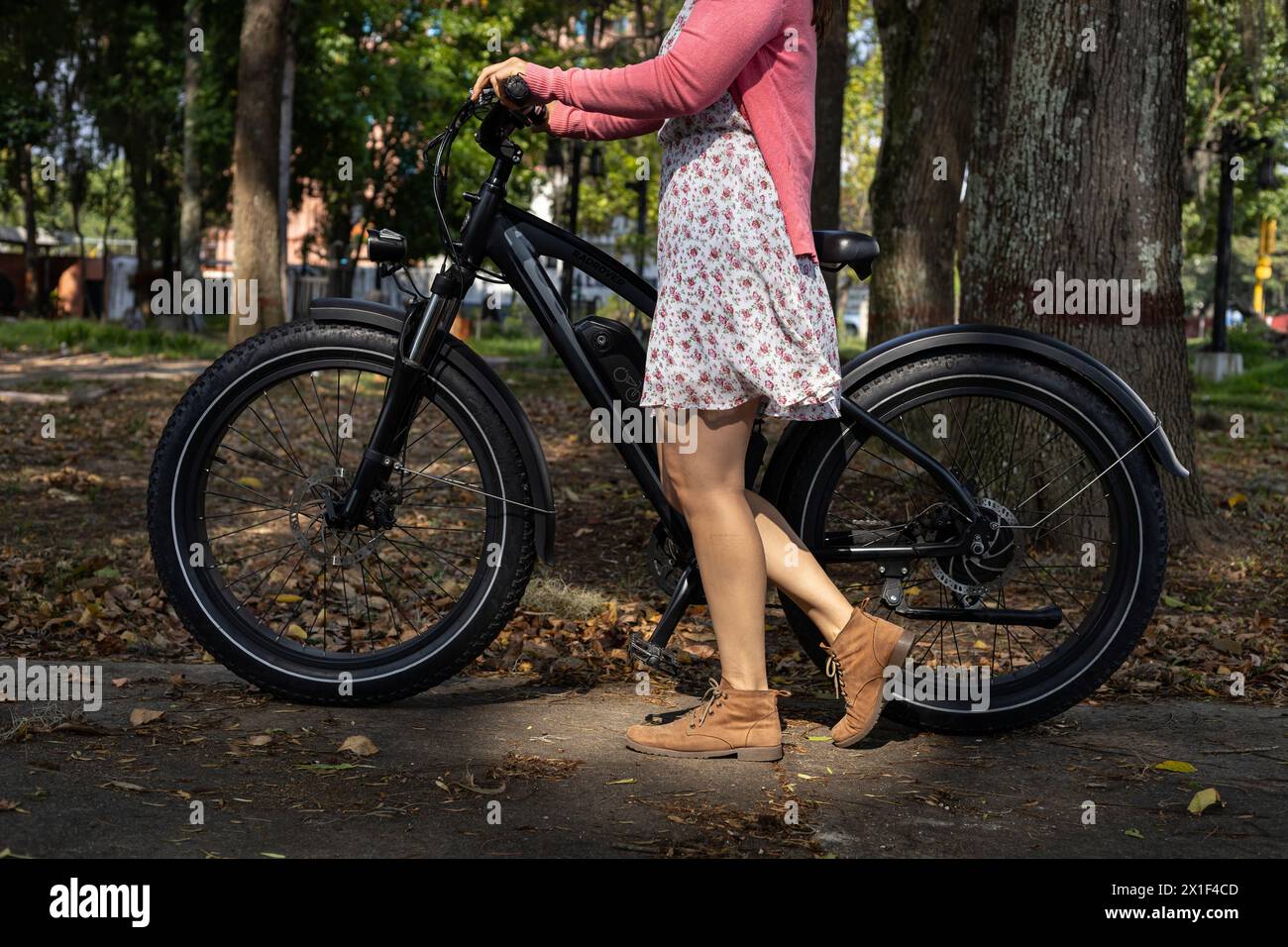 Junge Lateinamerikanerin (33) geht im Frühling mit ihrem Elektrofahrrad auf eine Fahrt. Konzeptmittel für Transport und Frühling. Stockfoto