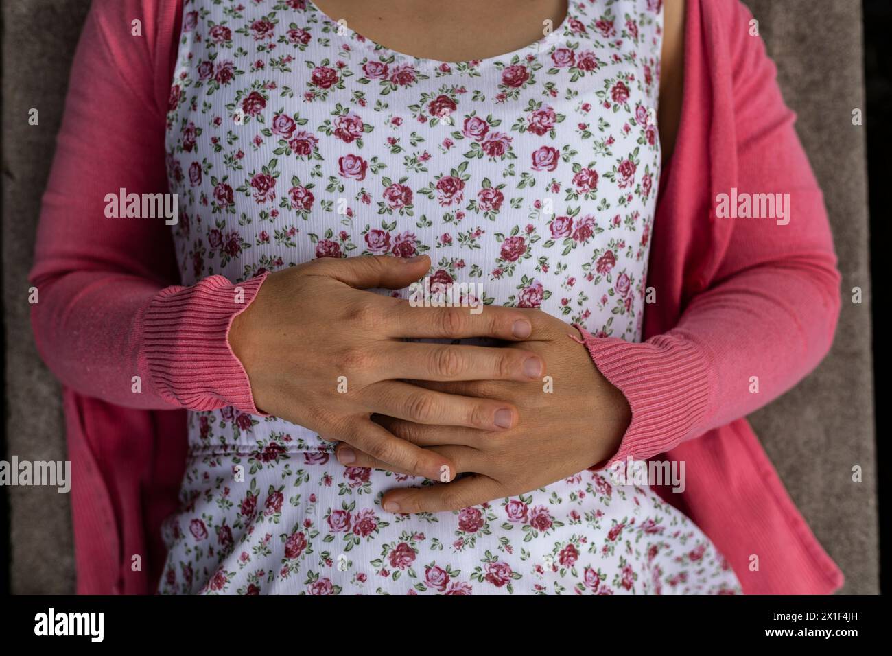 Blick von oben auf die Hände der jungen lateinamerikanischen Frau (33). Sie trägt ein Blumenkleid und einen rosa Pullover. Nicht erkennbar. Federkonzept. Stockfoto