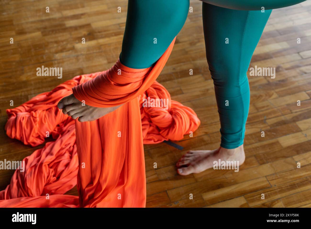 Junge lateinamerikanische Frau (33) in der Klasse mit Fluggymnastik-Stoffen lernt die Technik der Fußbindung, um sicher zu klettern. Yoga und Wellness Concep Stockfoto