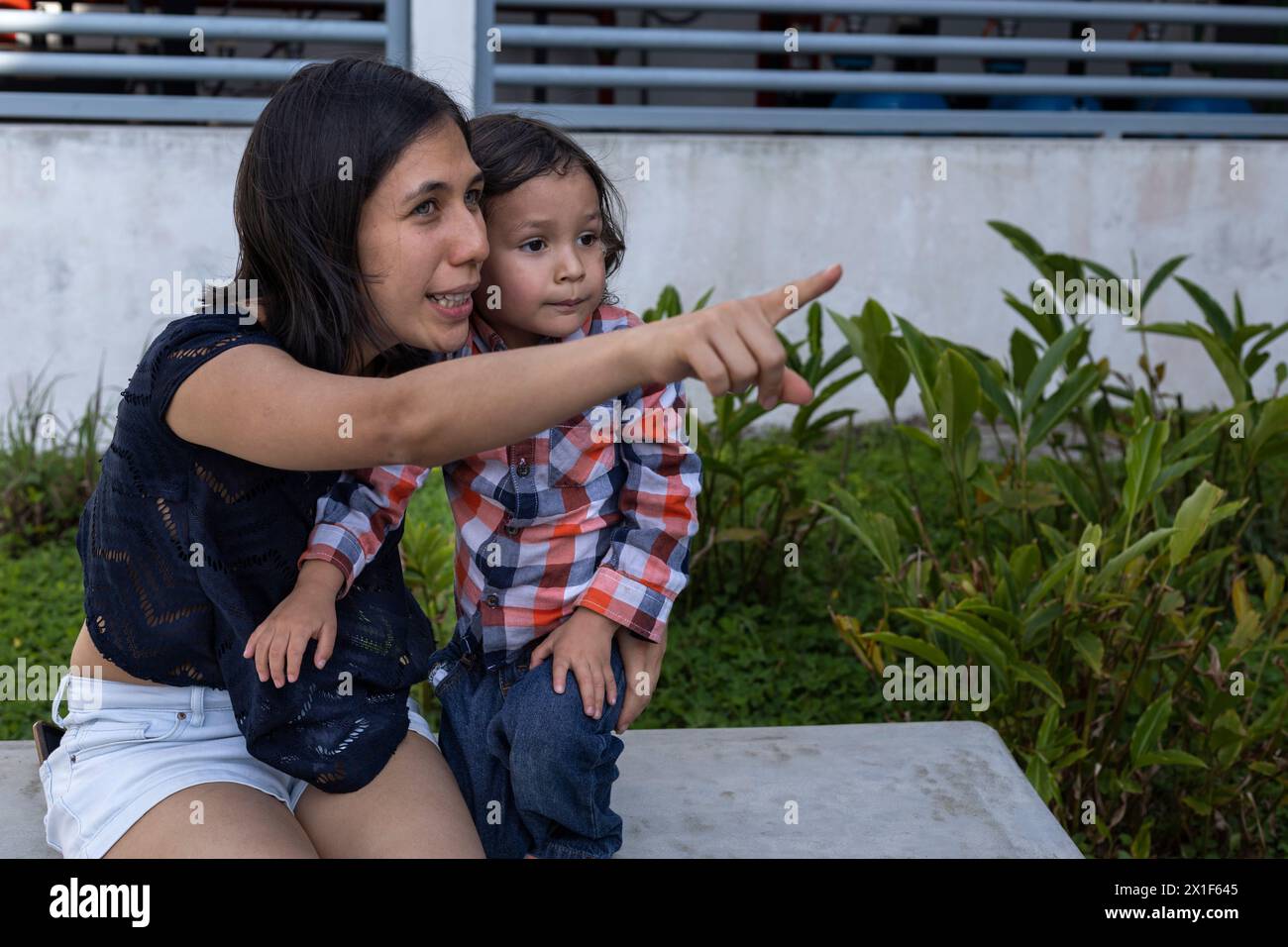Mom und ihr lateinamerikanischer Sohn sitzen auf einer Bank und zeigen ihre Liebe mit Lächeln und Glück. Muttertagskonzept und Familie Stockfoto