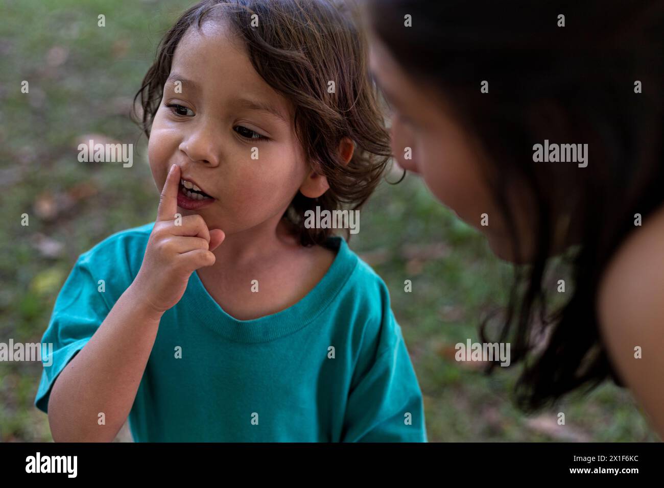 Die amerikanische Latina-Mutter hört die Bitte ihres dreijährigen Sohnes im Park. Familie und Muttertagskonzept. Stockfoto