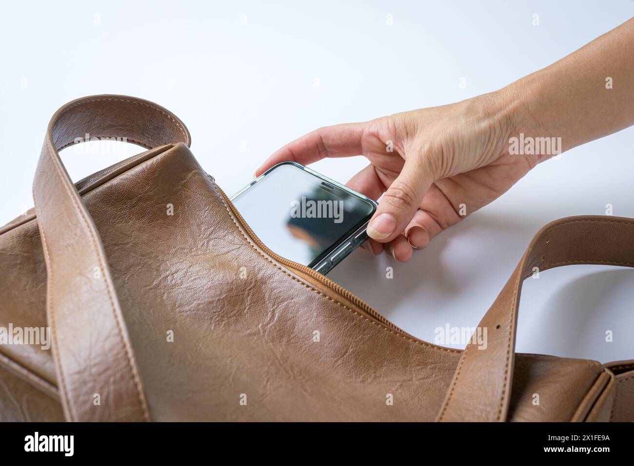 Die Frau hat das Handy in die braune Lederhandtasche gesteckt. Draufsicht. Stockfoto