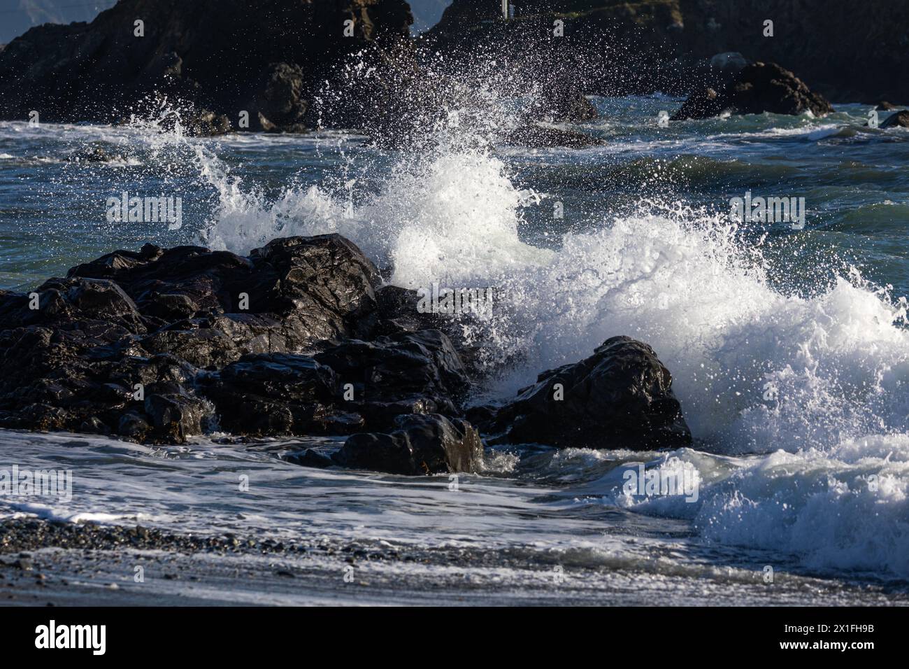 Das Meer ist rau und die Wellen stürzen gegen die Felsen. Das Wasser ist weiß und der Himmel blau Stockfoto