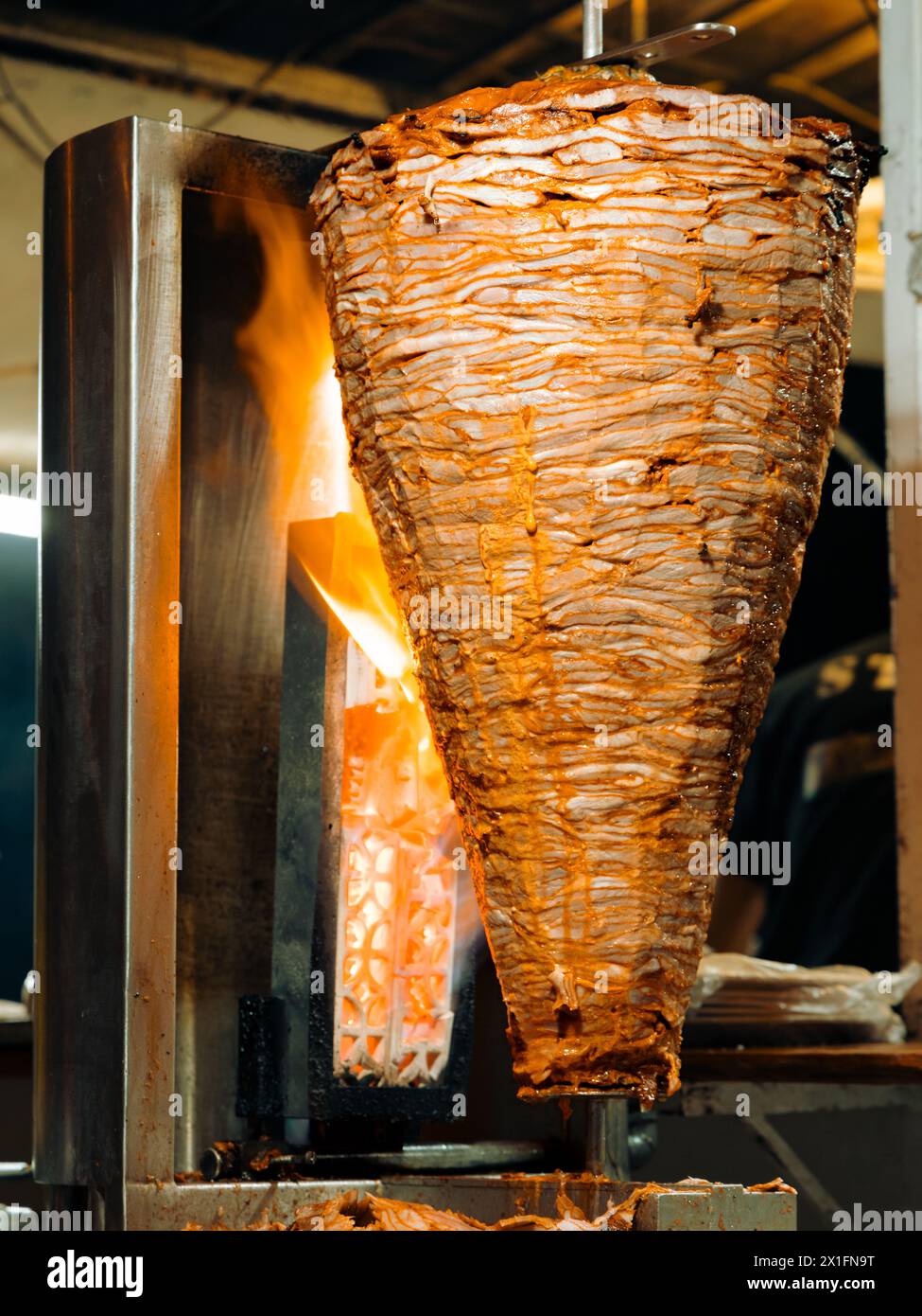 Vertikales Bild beim Grillen traditioneller Trompo al Pastor Street Taco Schweinefleisch auf Spieß mit Flammen nachts in Mexiko. Stockfoto